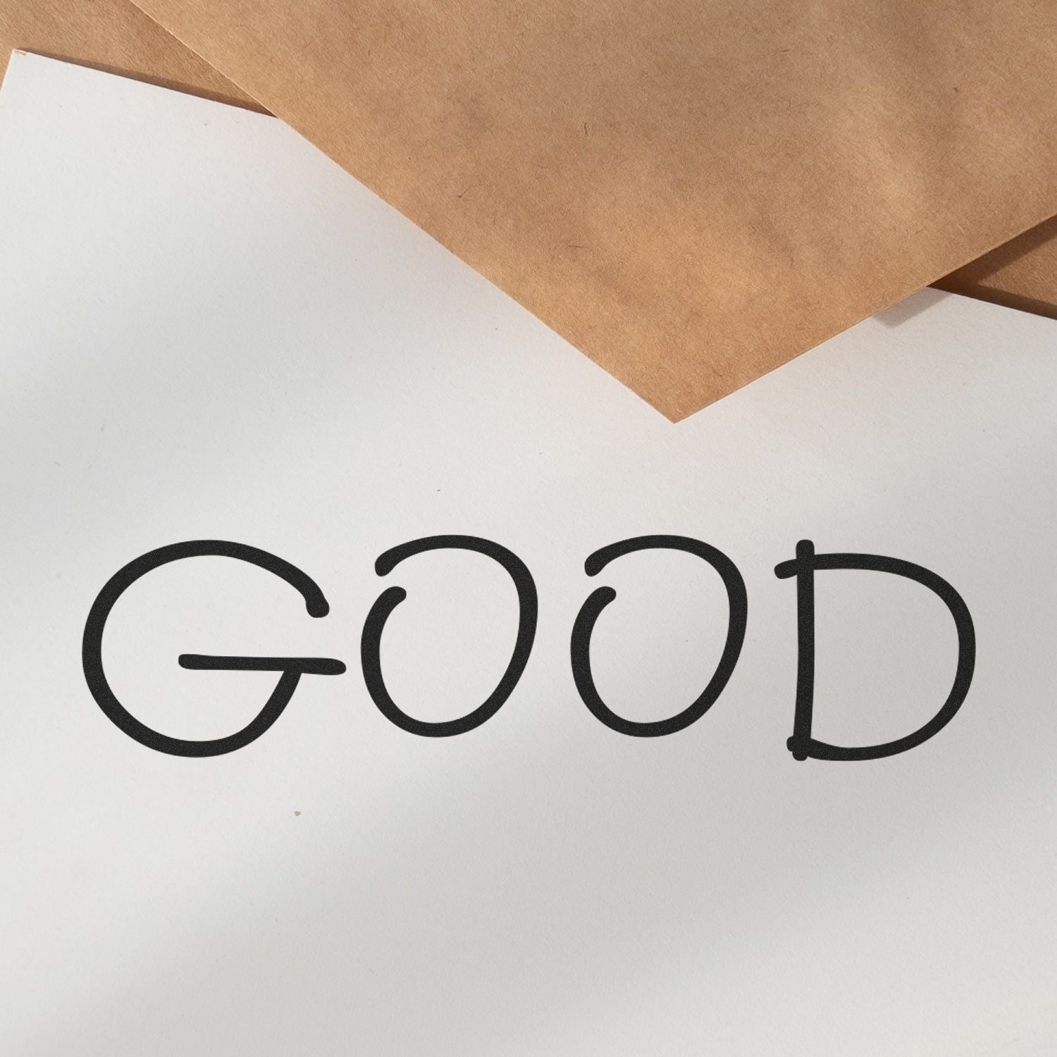 White label on kraft paper background with bold black GOOD lettering for greeting card, quote, or packaging design.