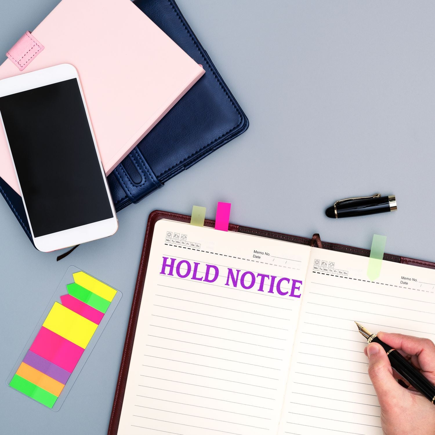 Overhead office desk with a Hold Notice notebook, smartphone, colorful sticky notes, and fountain pen for business planning and organization