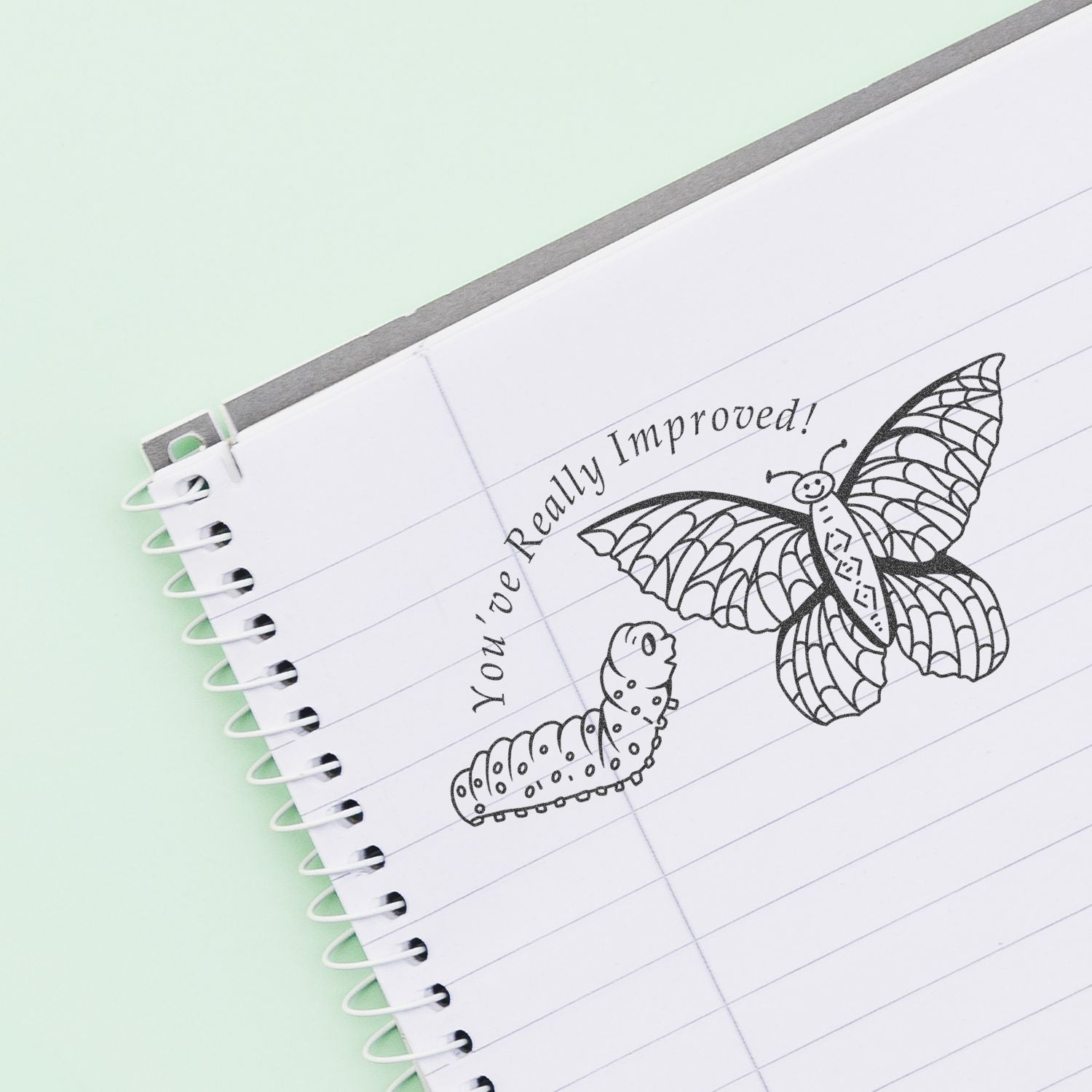 Lined notebook page with butterfly drawing and handwritten Youve Really Improved! message on a pastel background.