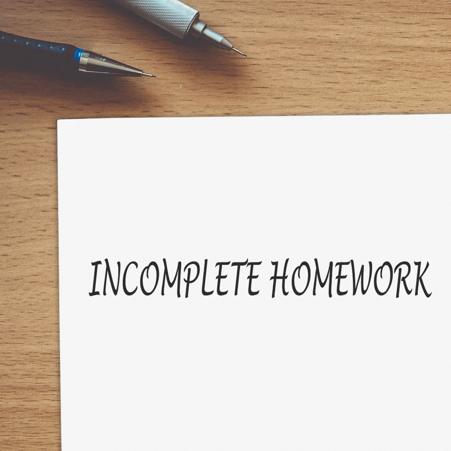 Two pens on a wooden desk beside a note reading Incomplete Homework, highlighting unfinished schoolwork and study reminders today.