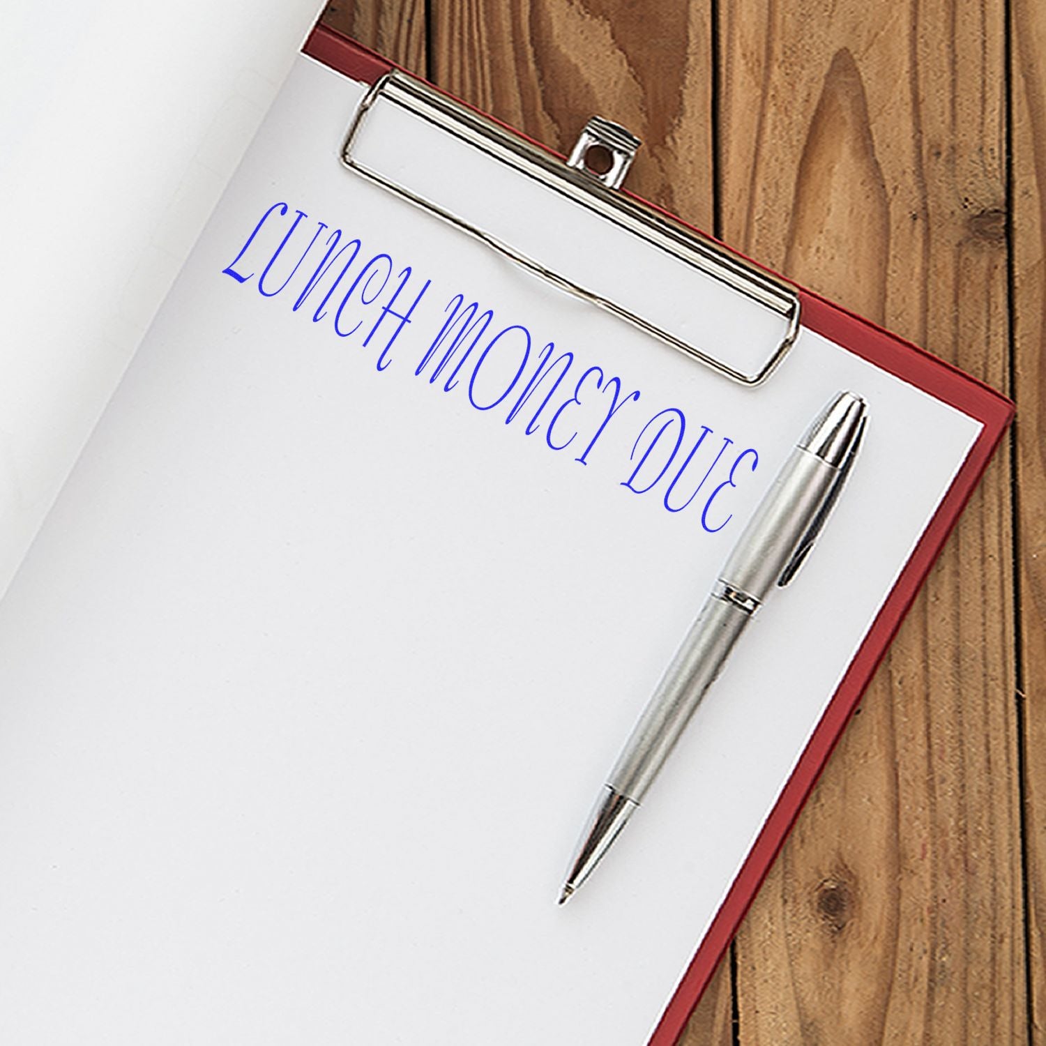 Clipboard with lunch money due note and pen on wooden desk.