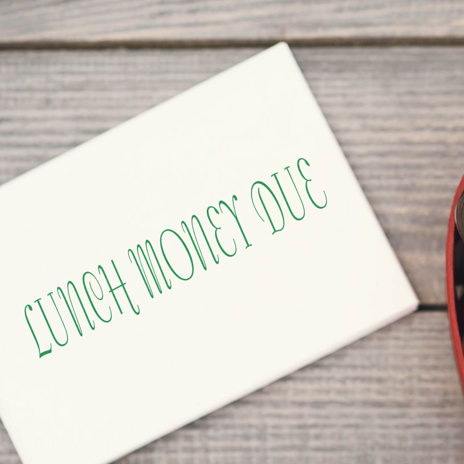 White envelope with green Lunch Money Due text on a rustic wooden background.