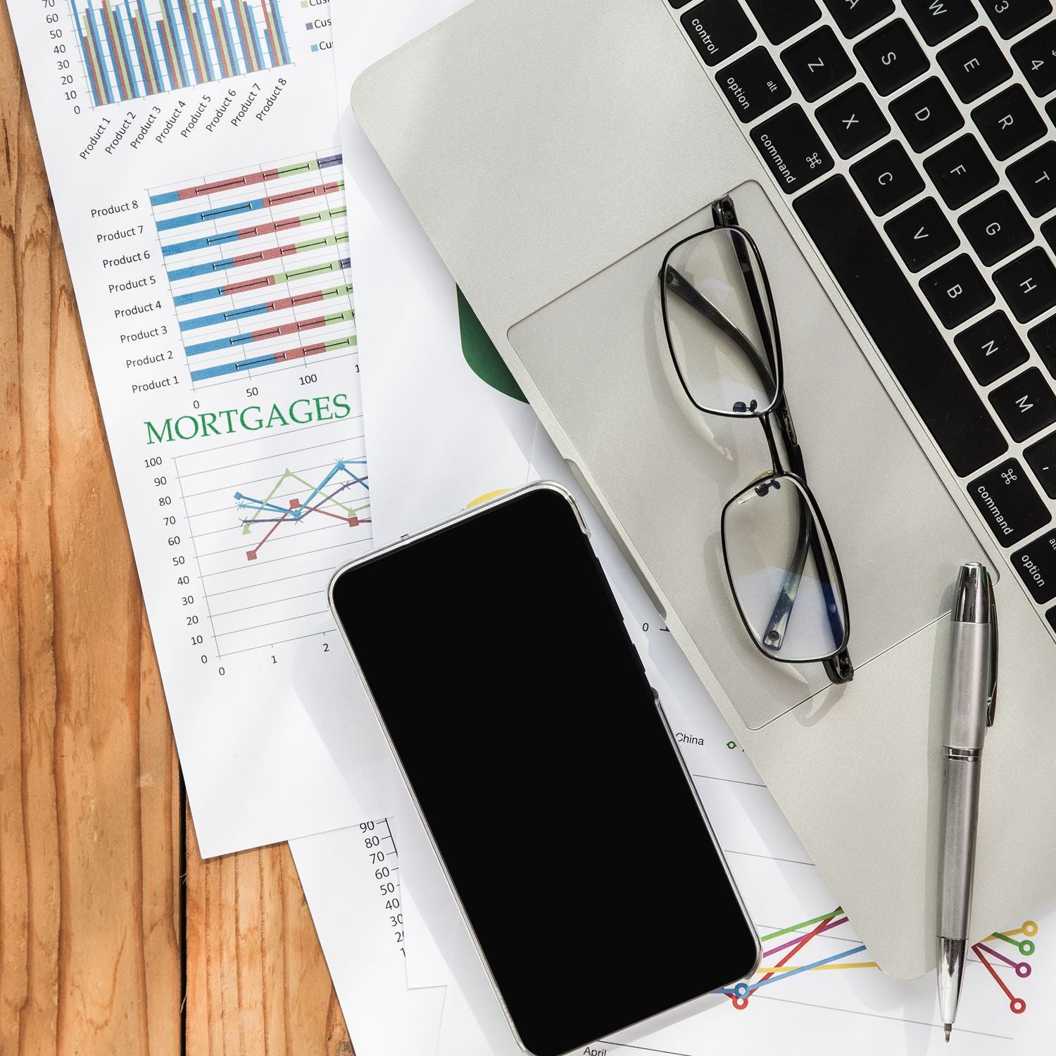 Financial data analysis desk with mortgages charts, laptop keyboard, smartphone, and pen for business reporting and forecasting.