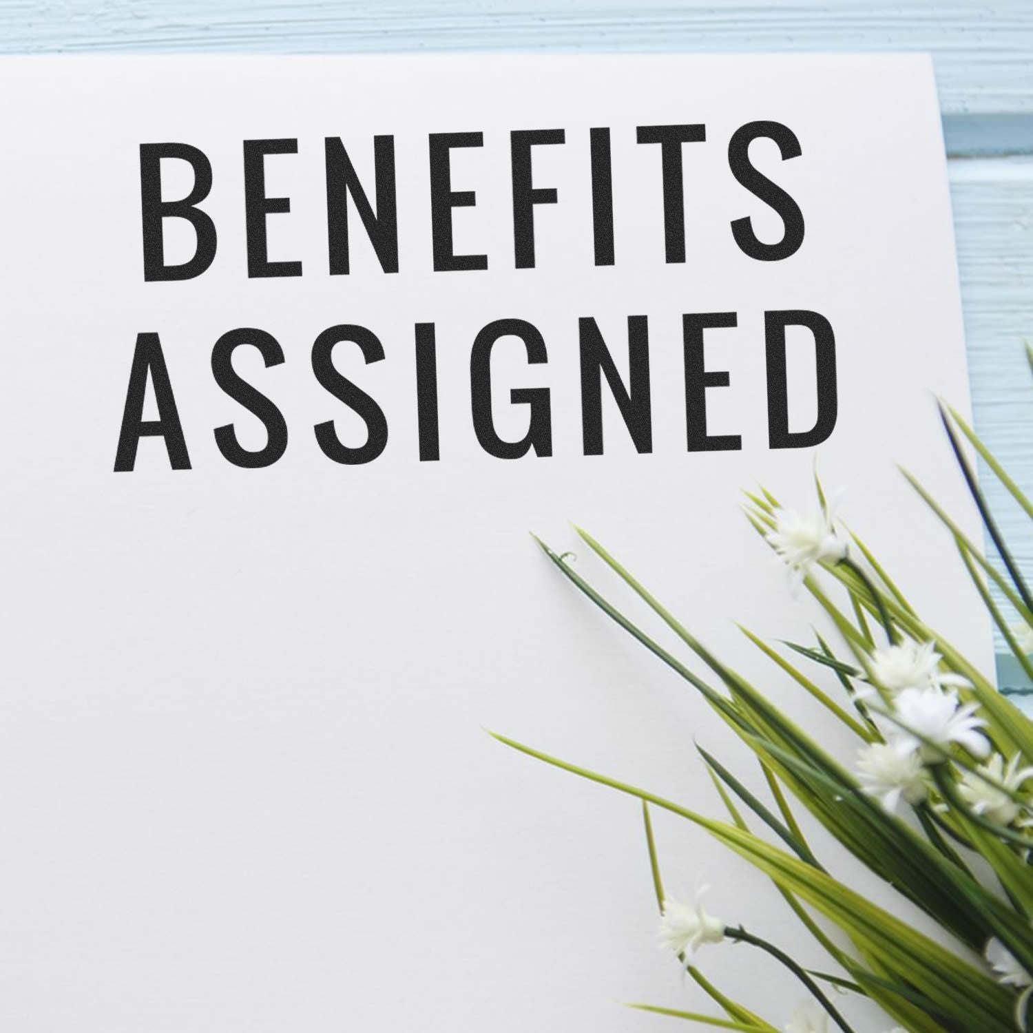 Card reading BENEFITS ASSIGNED with fresh white flowers and green stems, highlighting benefits and assignment information.