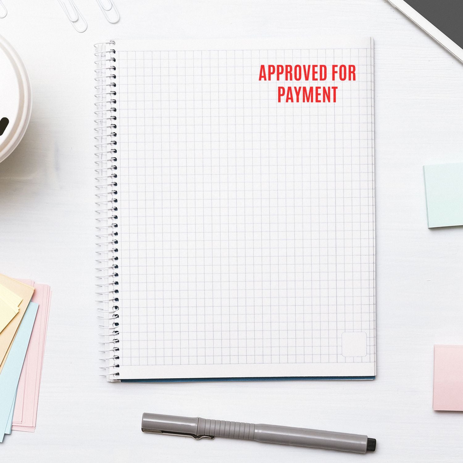 Approved for payment stamp on spiral notebook with office desk supplies.