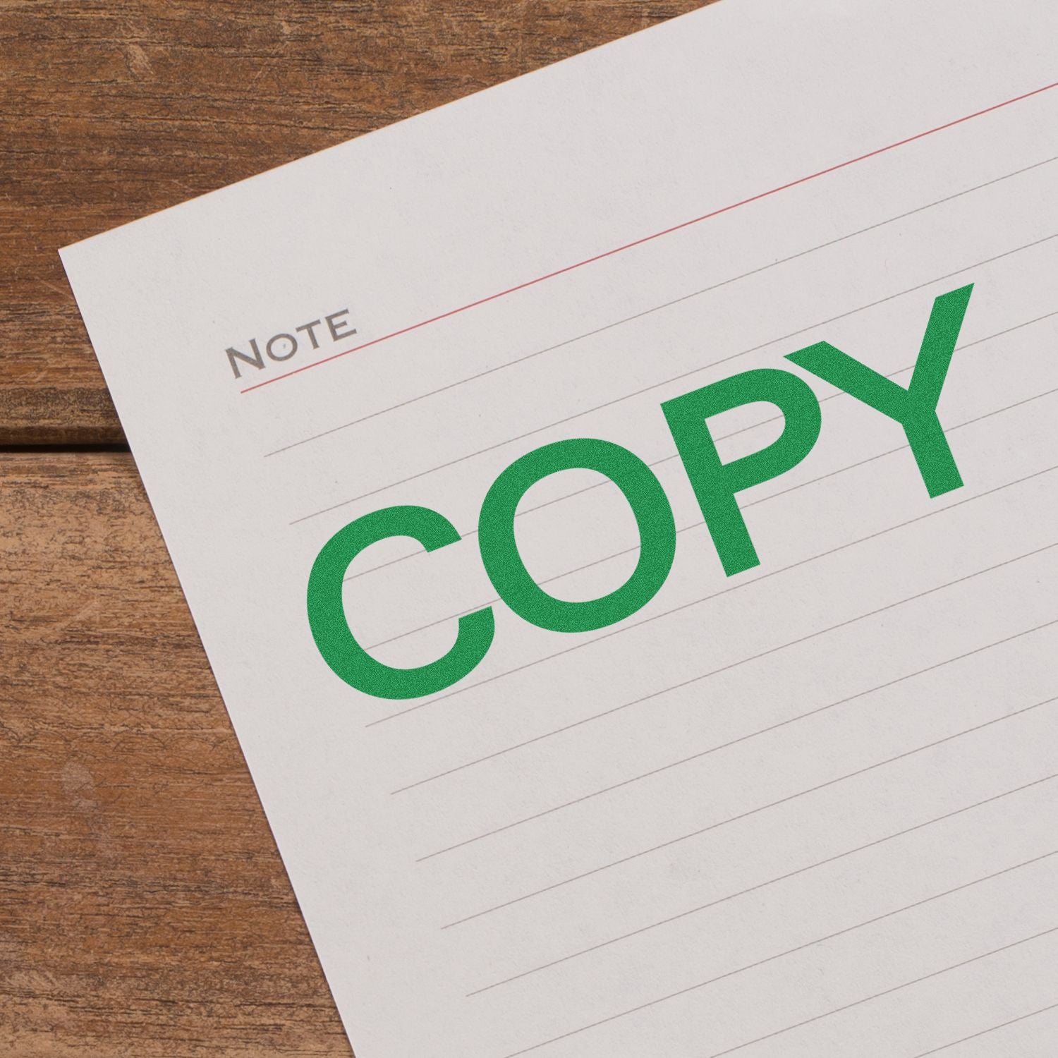 Close-up of lined note paper with green COPY text on a wooden desk.