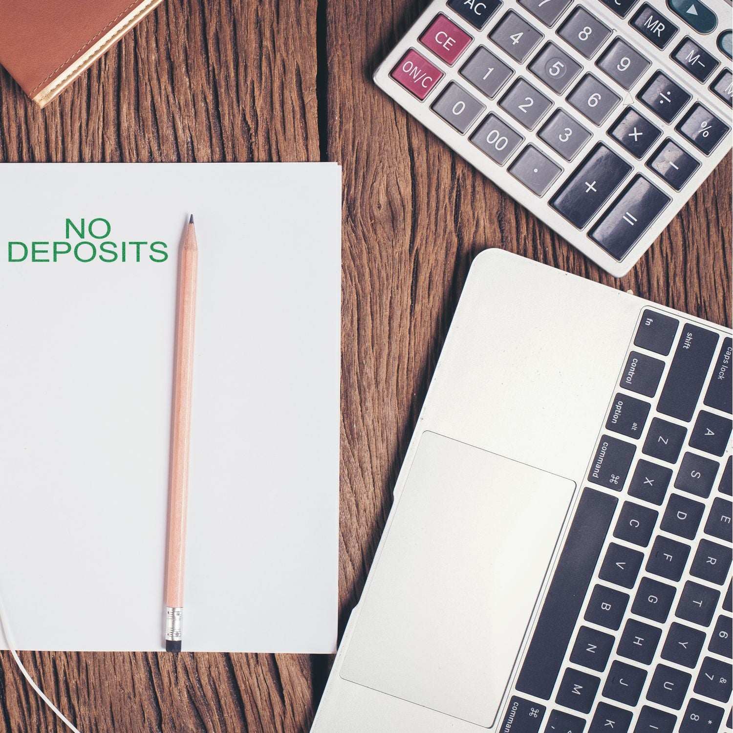 No deposits sign on notebook with pencil, calculator, and laptop on wooden desk for financial planning.
