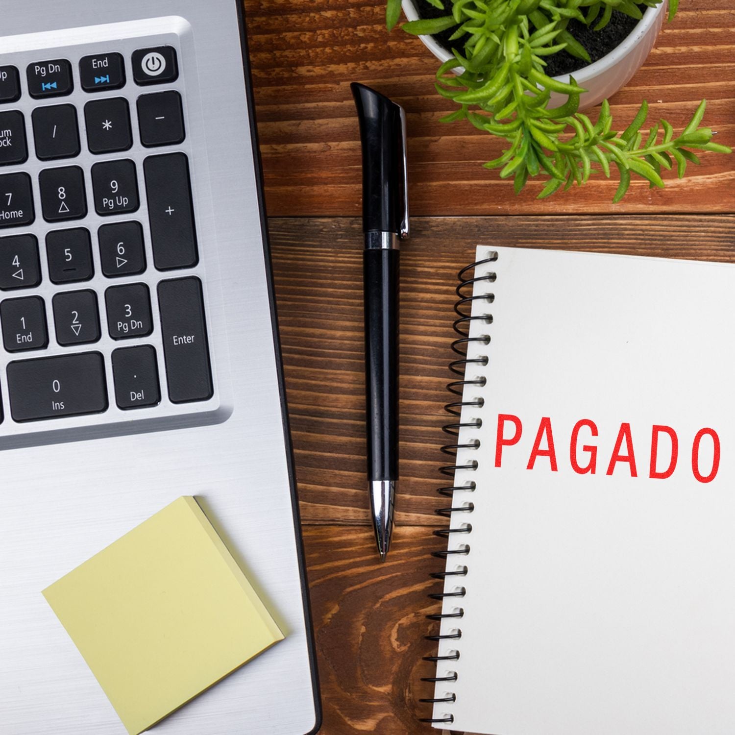 Laptop and pen beside notebook marked PAGADO, with payment documentation on a wooden desk for invoicing and accounting.