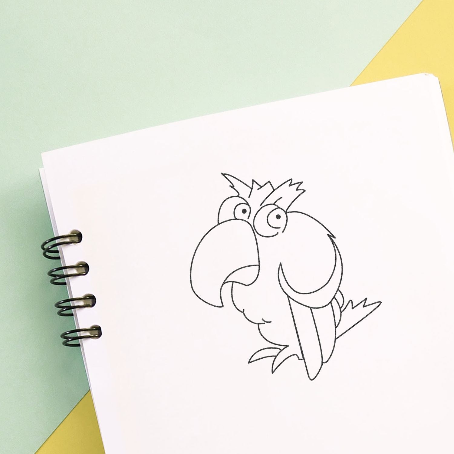 Spiral notebook with a cute hand-drawn parrot coloring page on a pastel background.