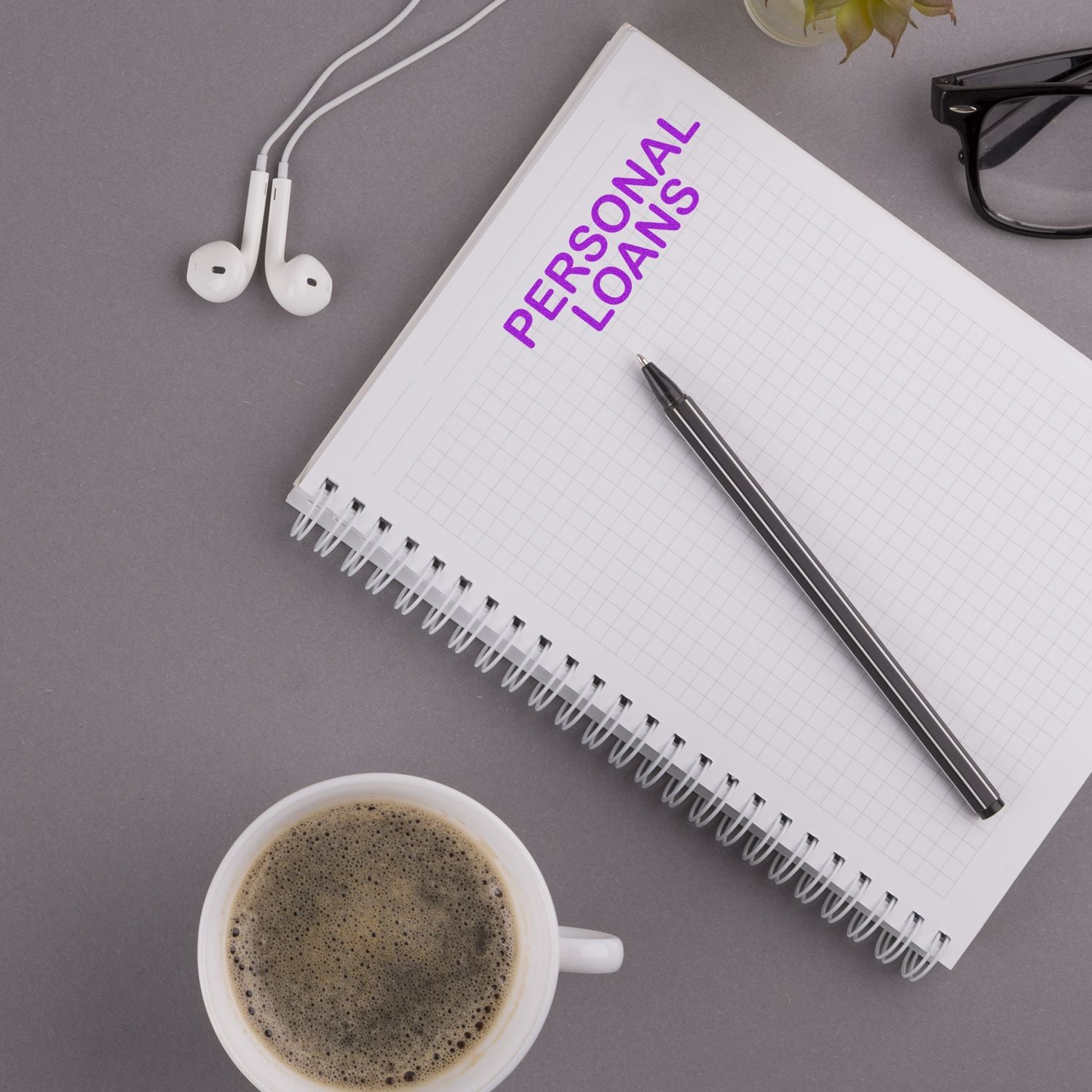Personal loans concept with notebook, pen, coffee cup, and earbuds on a desk, representing finance and budgeting.