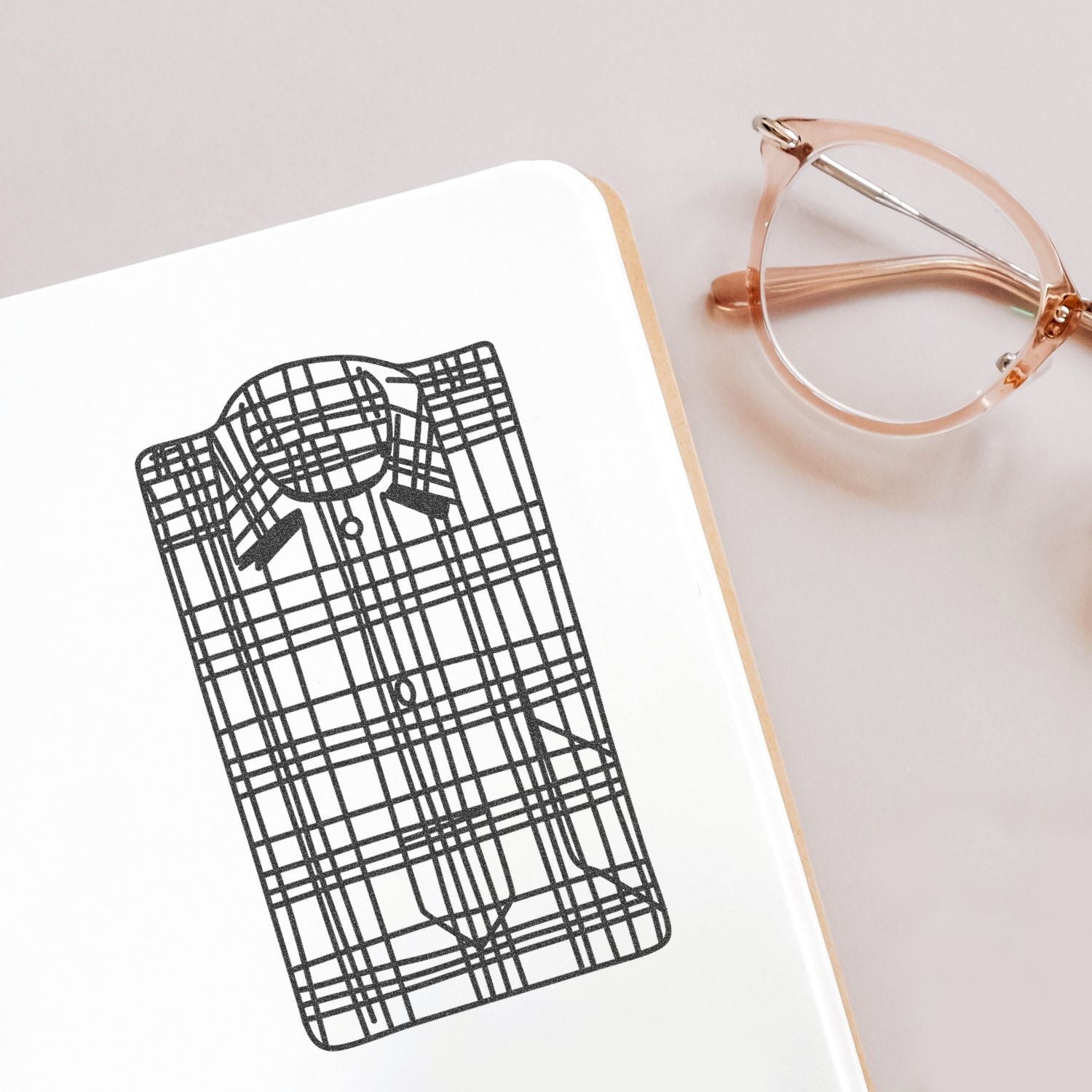 Plaid shirt illustration on a notebook next to rose gold eyeglasses on a clean desk background.