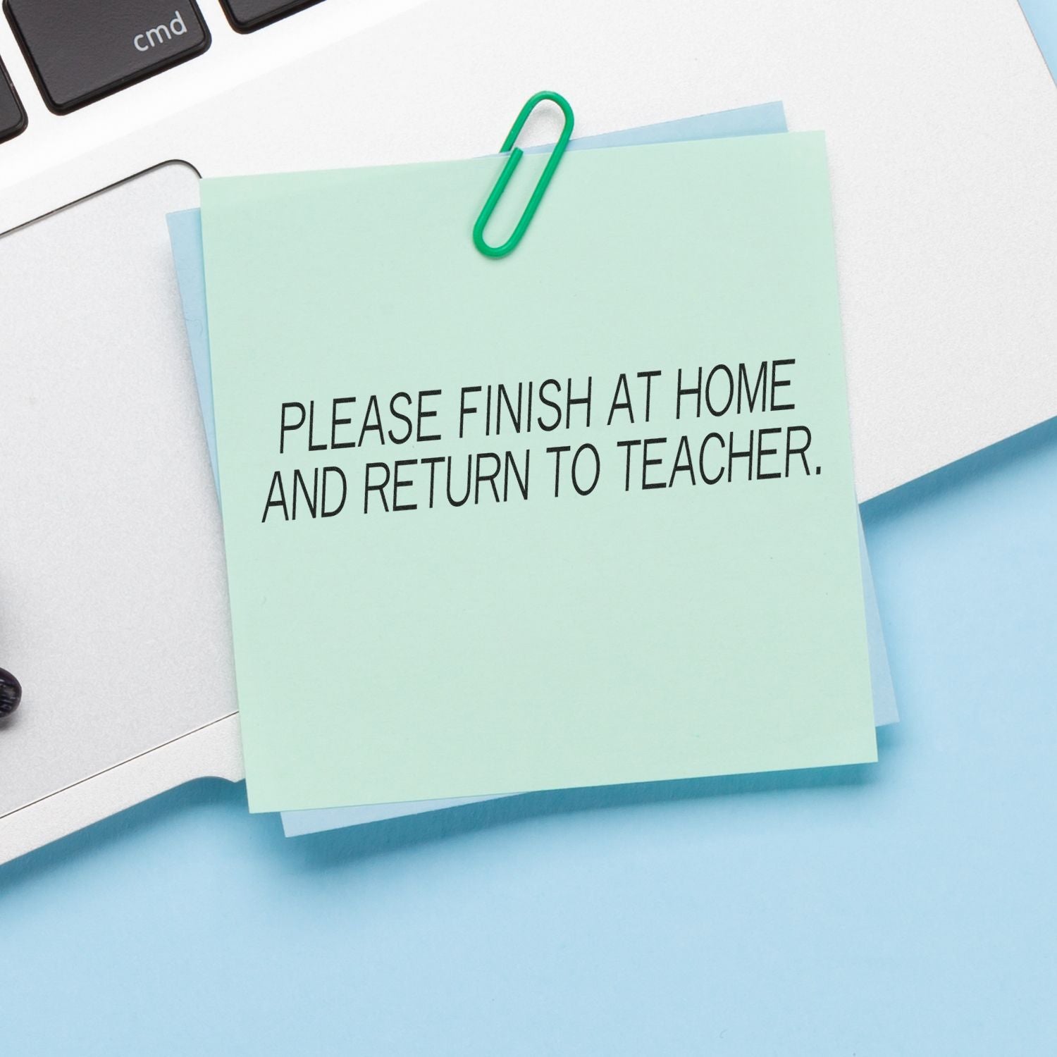 Student homework reminder note on desk: Please finish at home and return to teacher, with binder clip for submission.