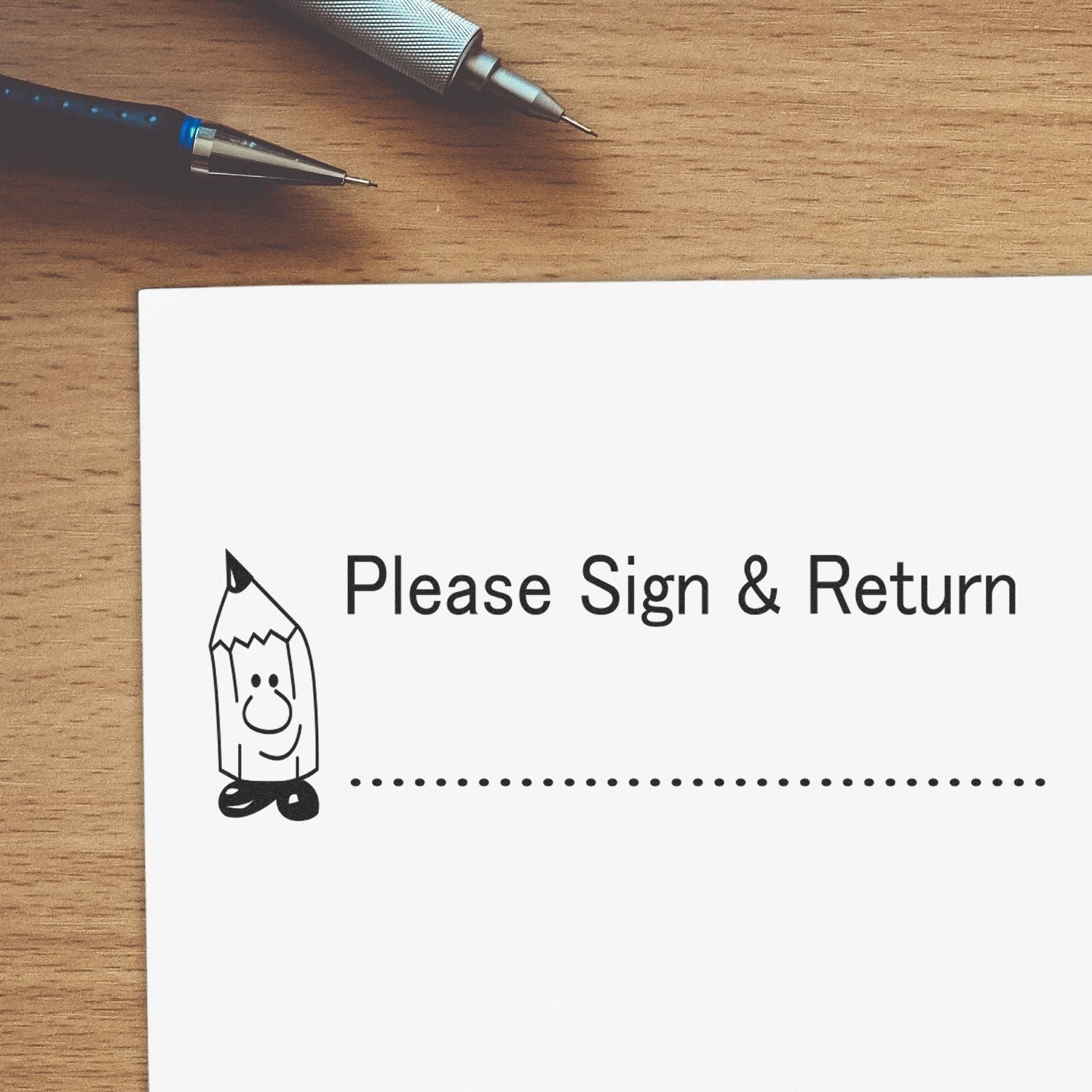 Wood desk with pens beside Please Sign & Return note, indicating document signature and return request for contracts, forms, or paperwork.