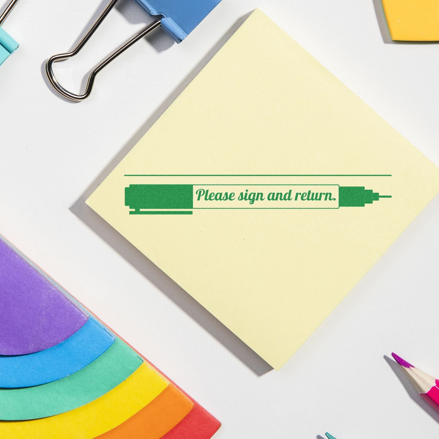 Colorful office stationery with sticky note reading Please sign and return on a white desk, surrounded by paper clips, pencil, and notes.