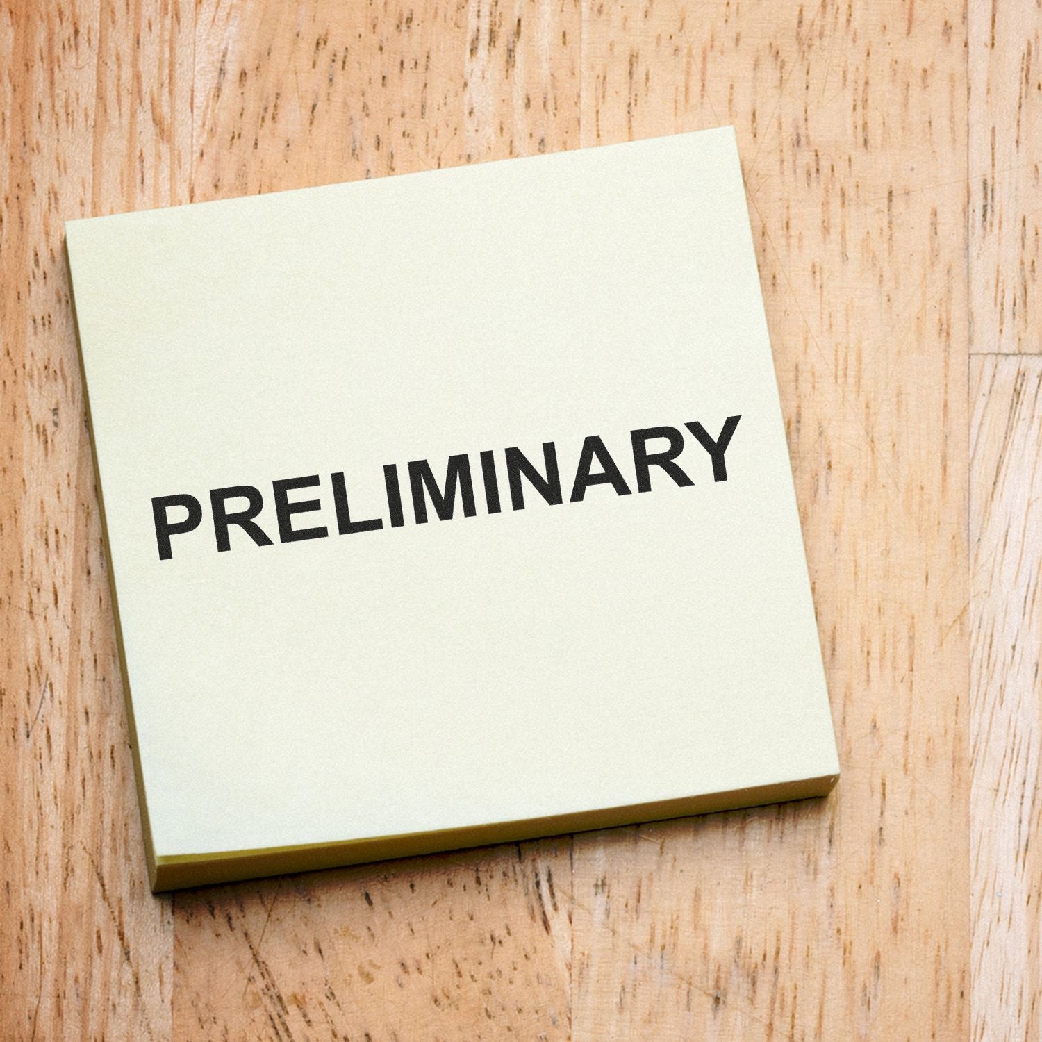 Preliminary sticky note on a wooden background, concept of draft or initial review.