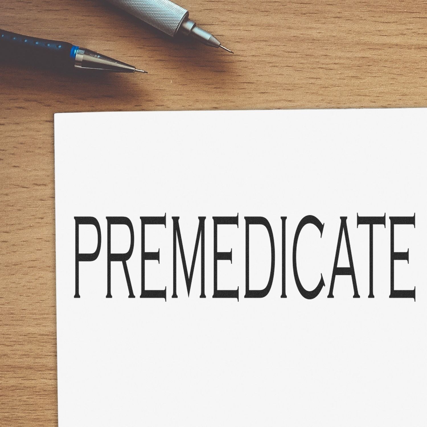 Word PREMEDICATE printed on paper with two pens on a wooden desk.