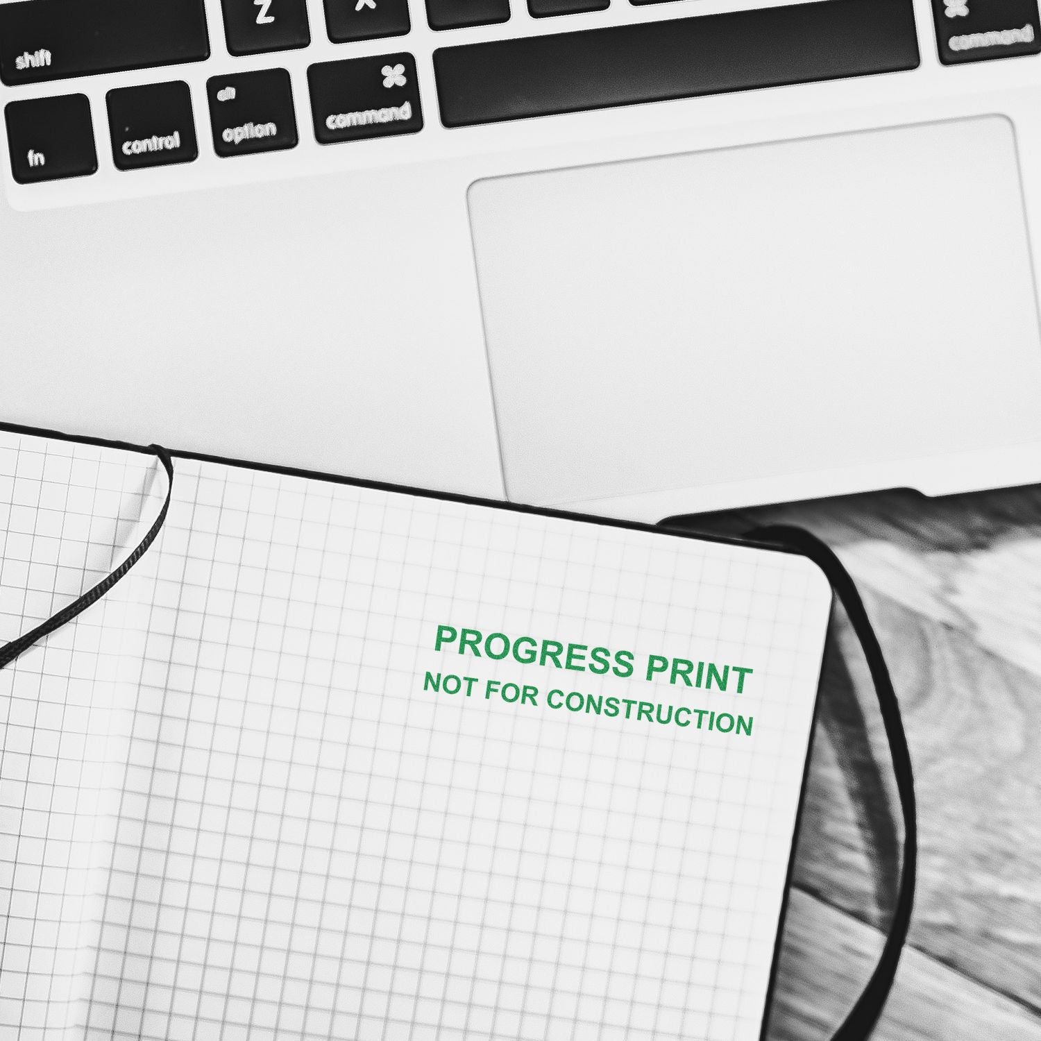 Laptop keyboard beside a notebook labeled Progress Print Not for Construction on a desk.
