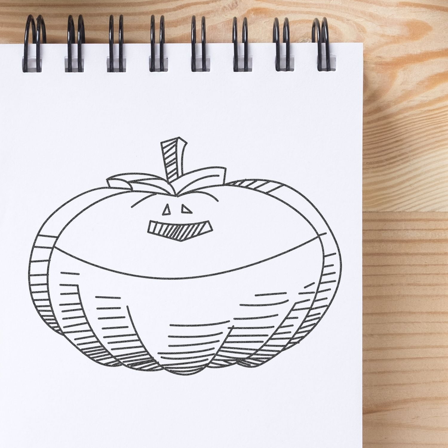 Black line pumpkin sketch in a spiral notebook on a wooden desk, Halloween drawing illustration.