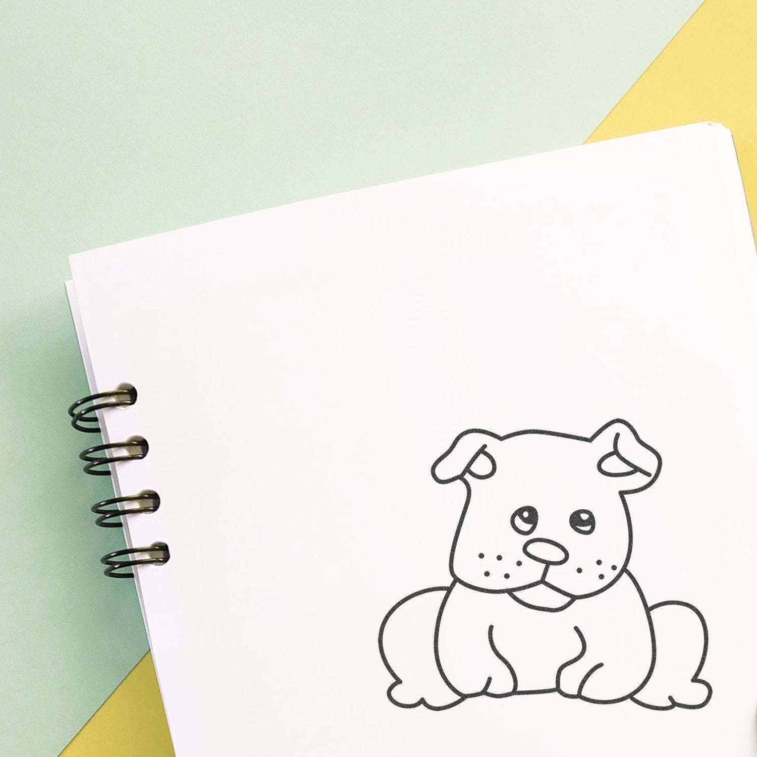Cute puppy coloring page in a spiral notebook on a pastel background.