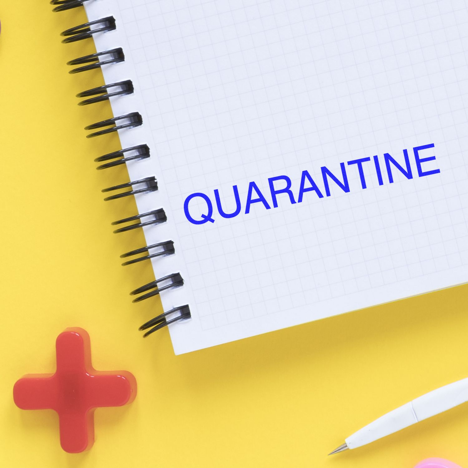 Quarantine concept with notebook, medical red plus symbol, and pen on yellow background.