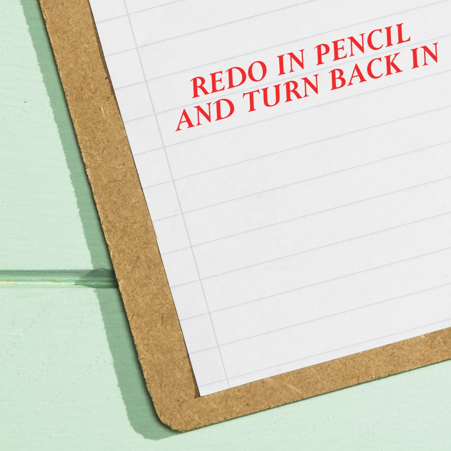 Clipboard with lined notebook paper reading Redo in pencil and turn back in in red text, school assignment note.