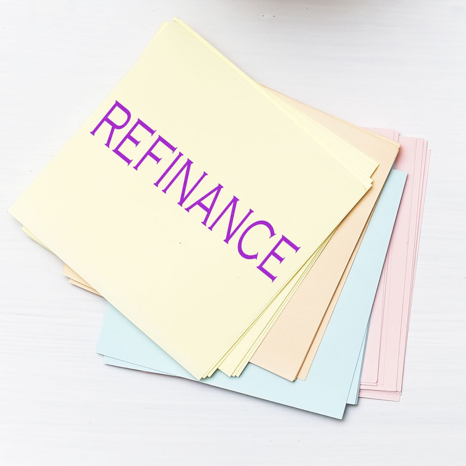 Stack of pastel loan refinance documents with bold purple REFINANCE text on top