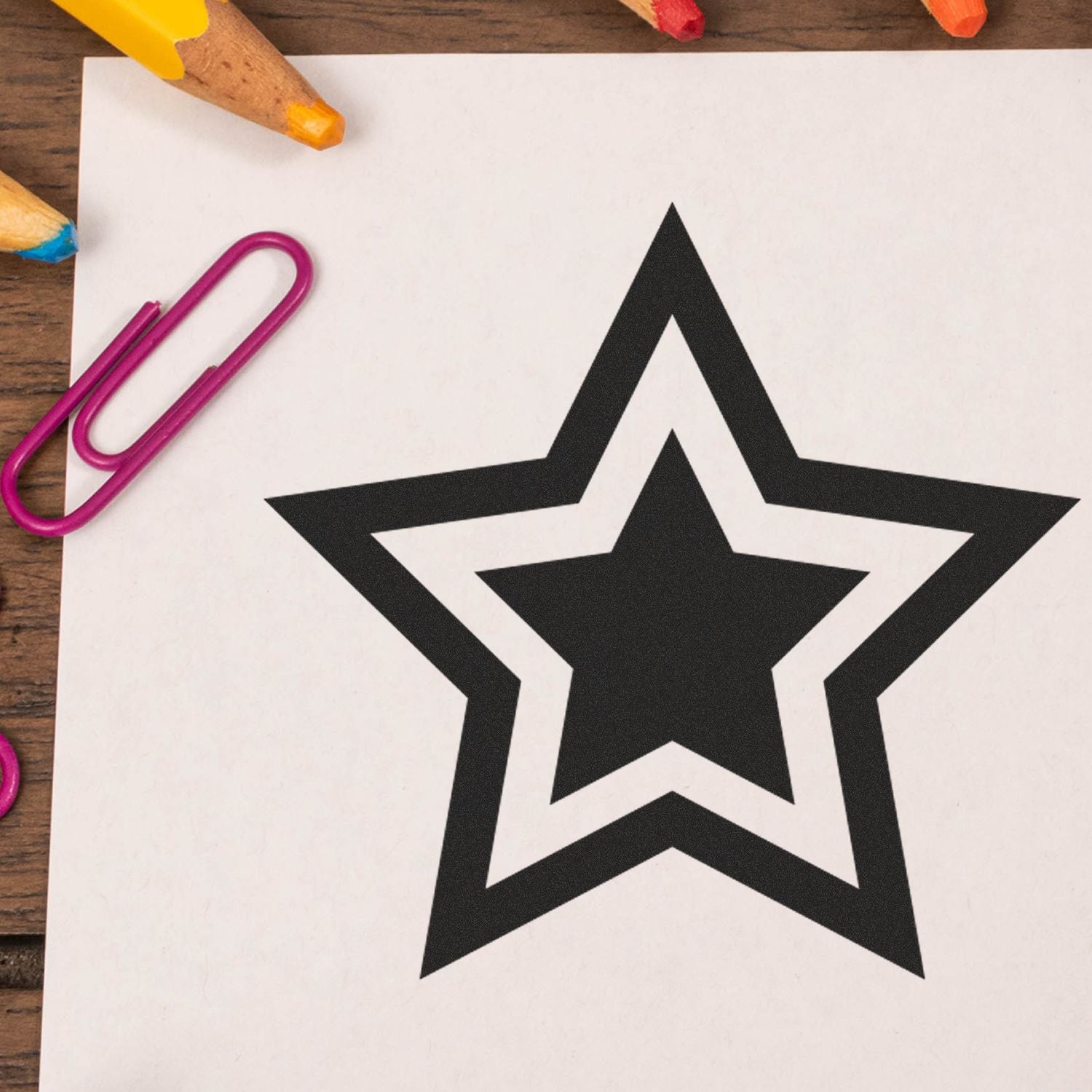 Black double star outline printable on white paper with colored pencils and paper clips on a wooden desk.