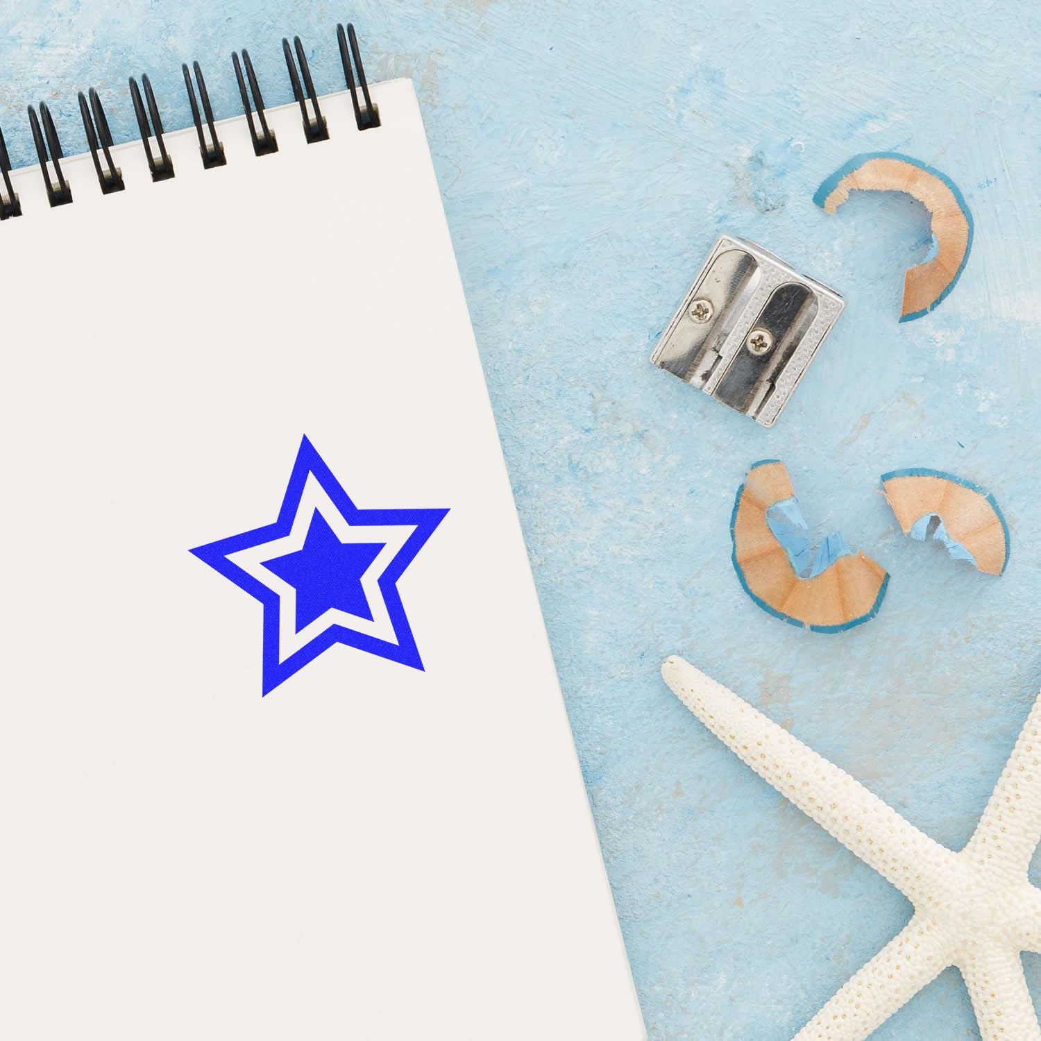 Spiral notebook with blue star logo, pencil sharpener, and starfish on light blue background