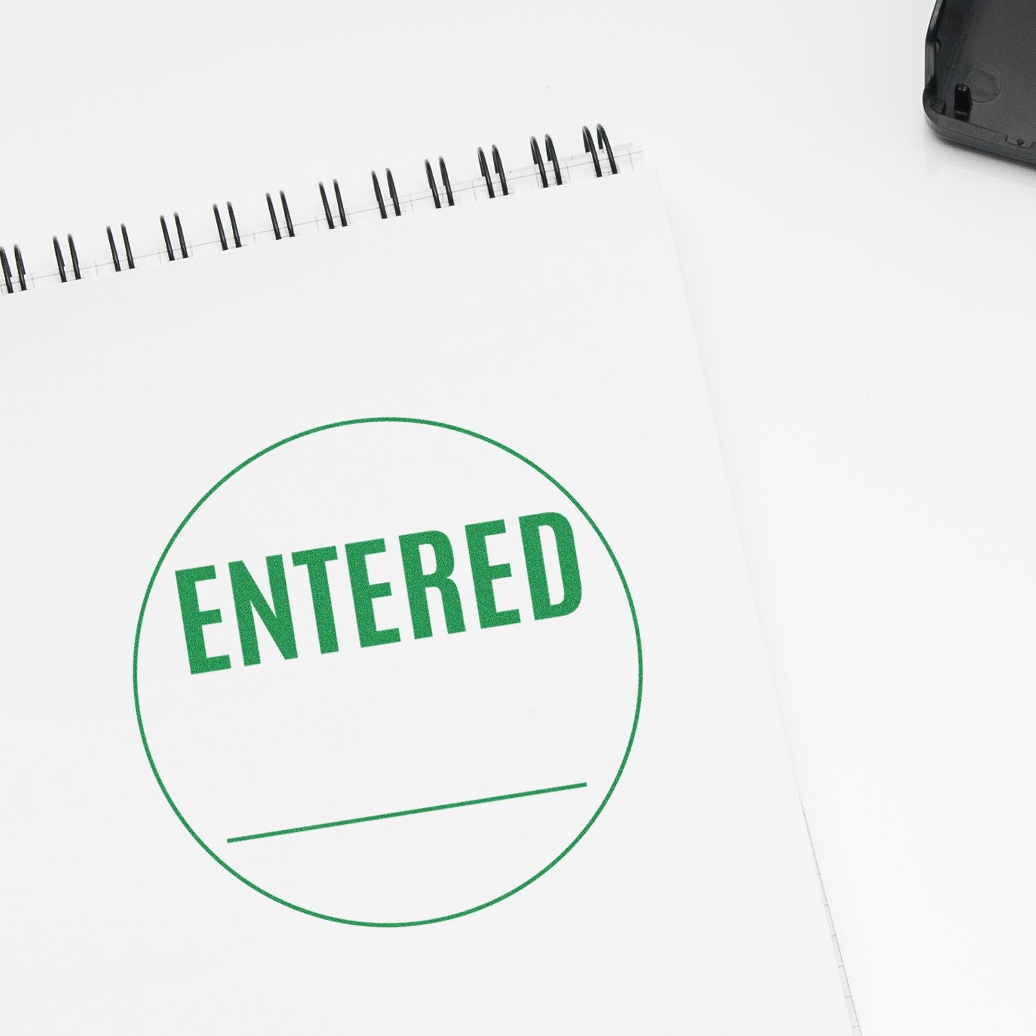 Green ENTERED stamp on a blank spiral notebook page, business concept of approval, records, or entry confirmation.