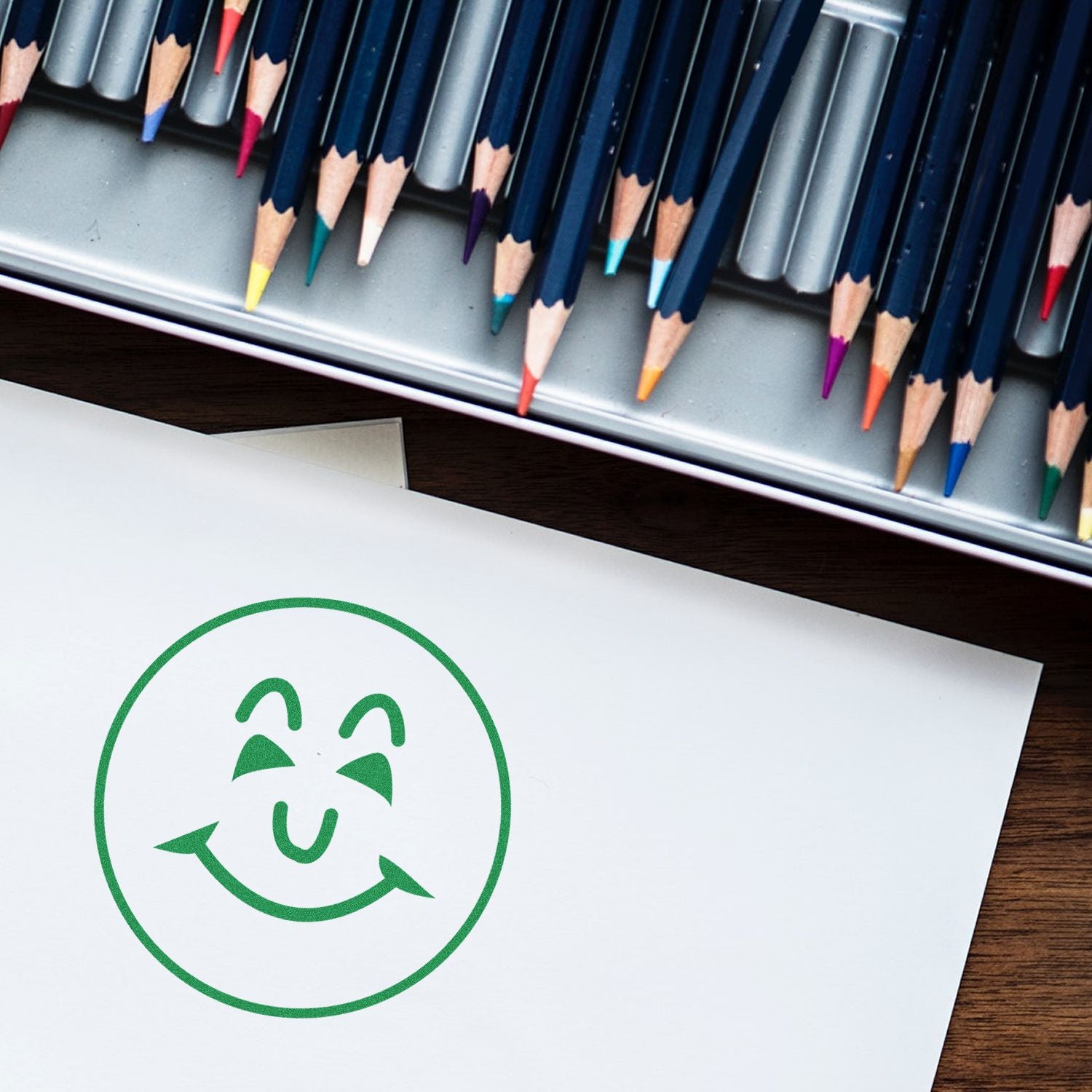 Green recycling symbol on white paper beside colored pencils, eco-friendly creative concept.