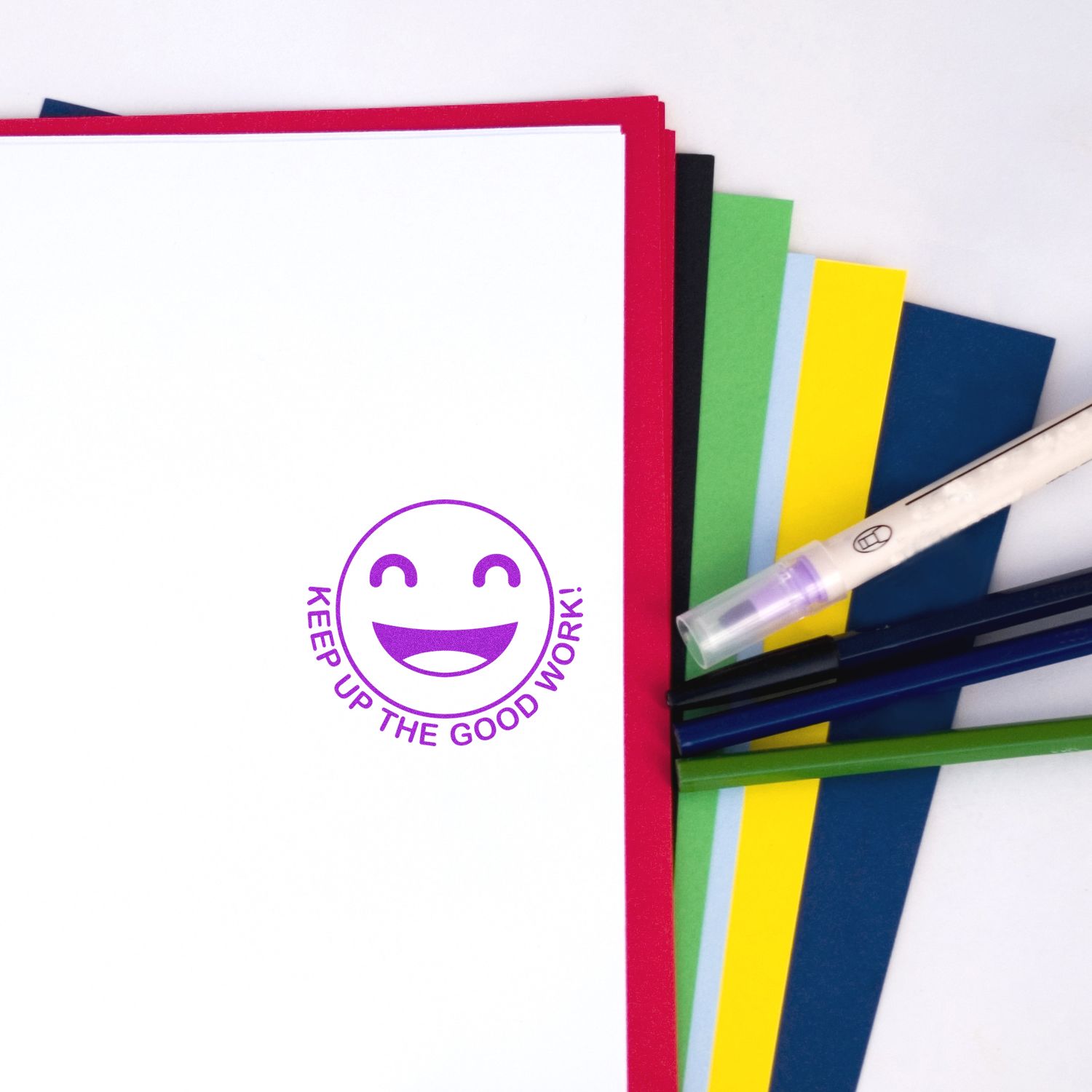 Colorful stationery set with notebooks, pens, and a Keep Up the Good Work smiley design on a white background.