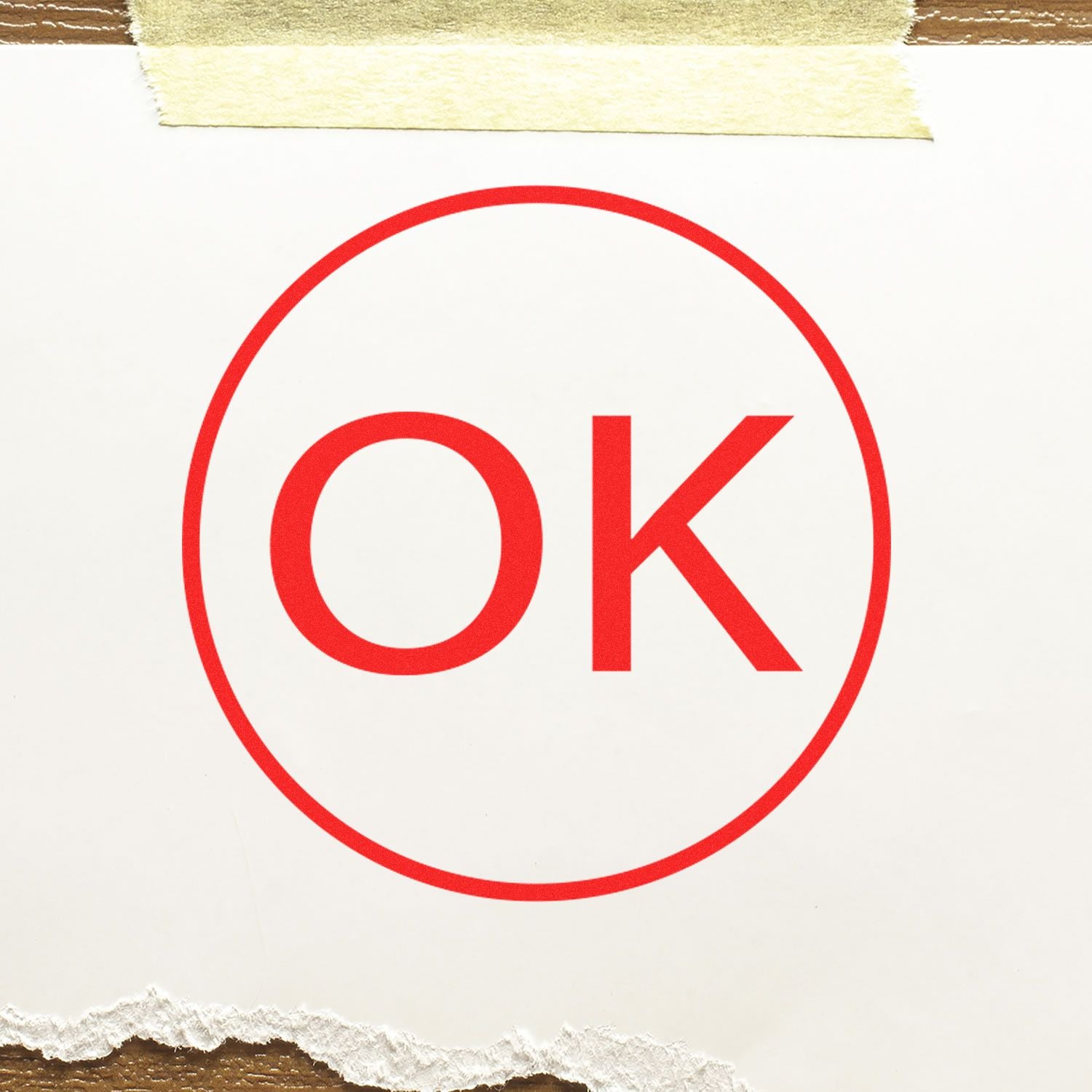 Red OK approval stamp in a red circle on white paper taped to a wooden background.