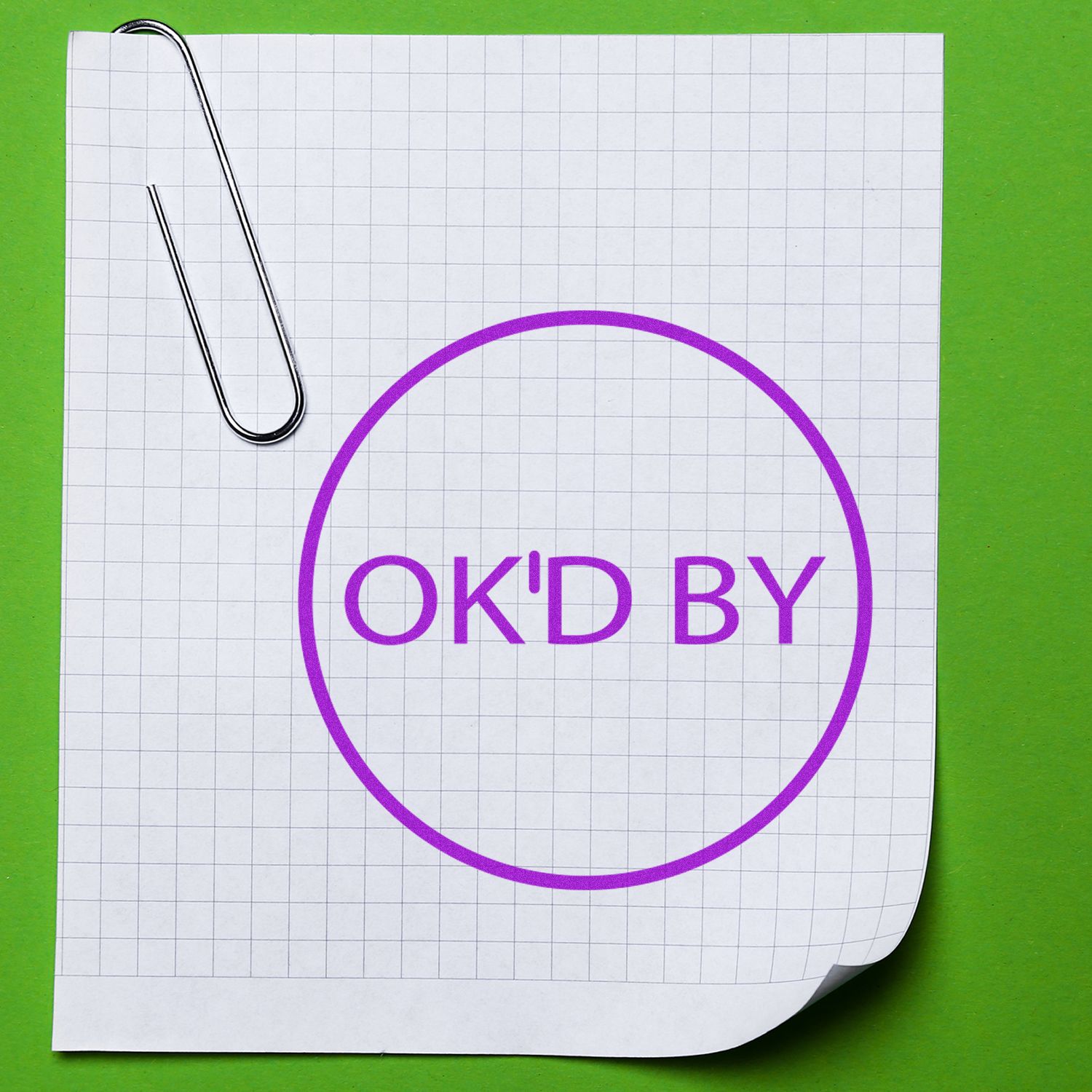 Paper clip holding graph paper with purple OKD BY stamp on a green background