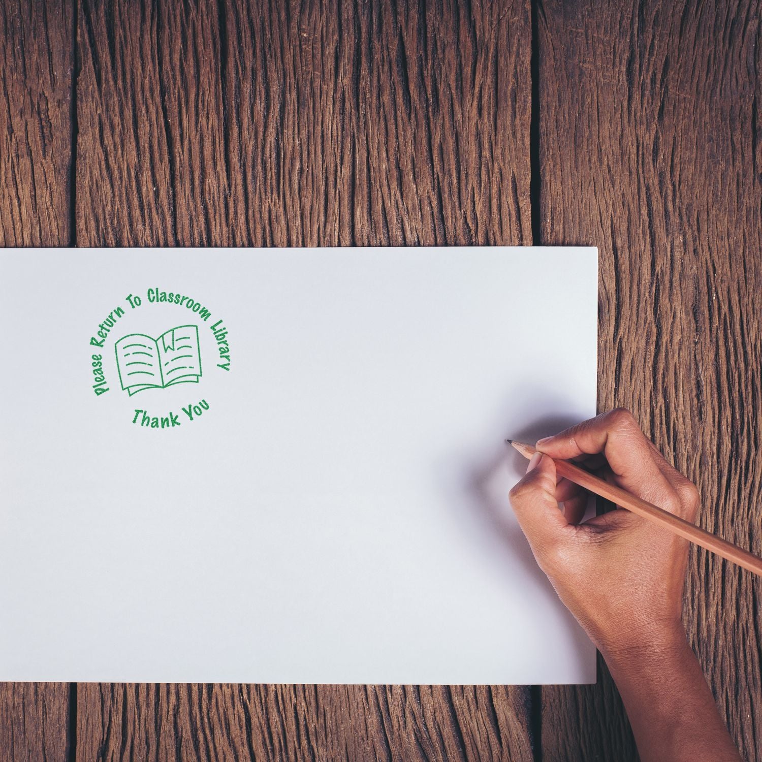 Hand writing on a white sheet with Please Return to Classroom Library stamp on a wooden desk, school supply and education concept.