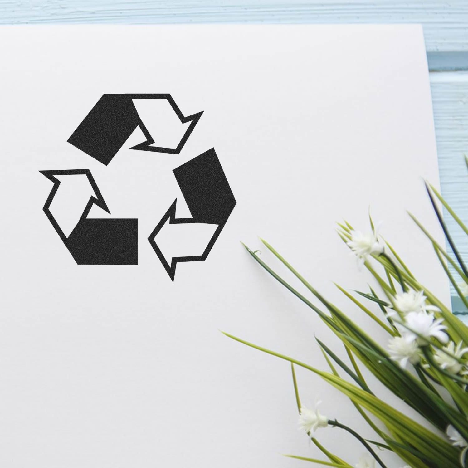 Black recycling symbol on white paper with green flowers, eco-friendly recycling concept, sustainable design icon.