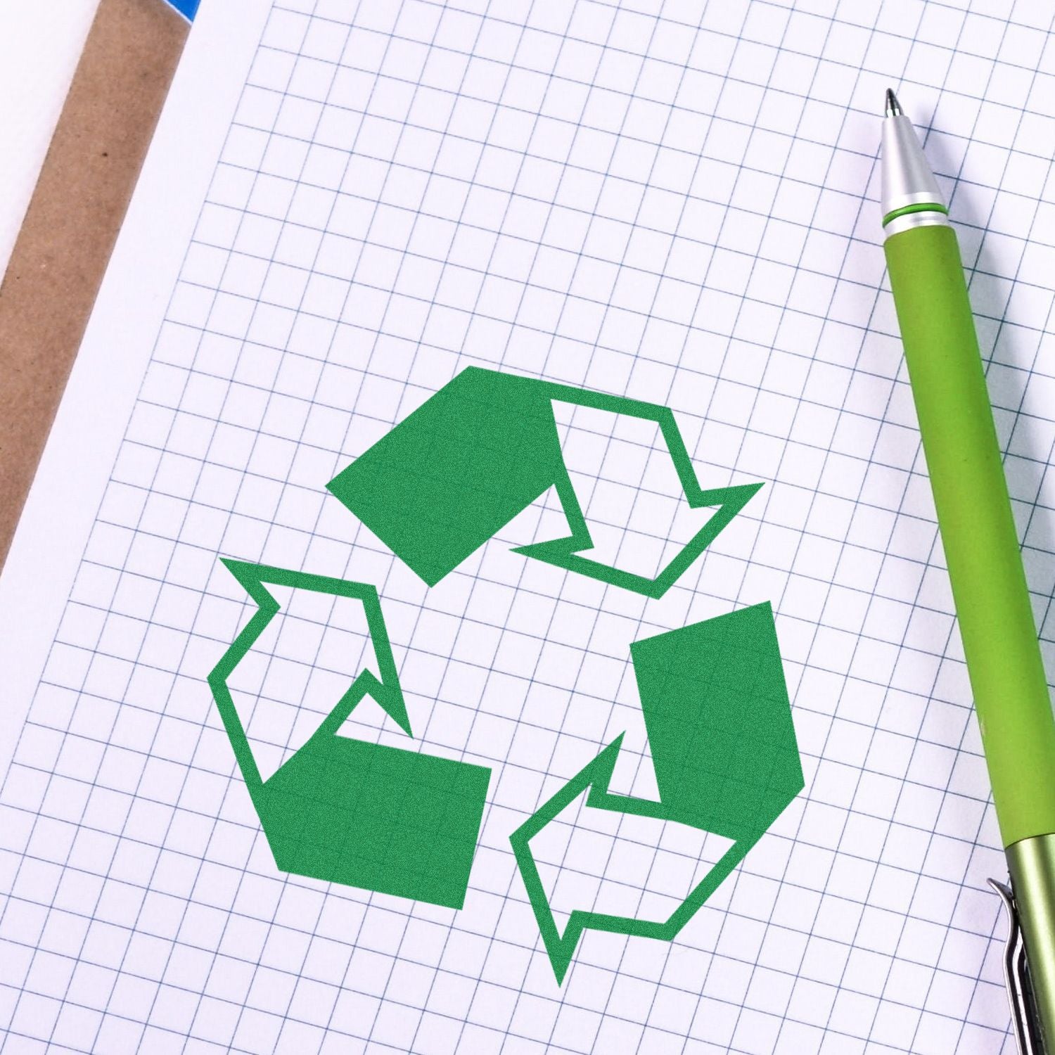 Green recycling symbol on graph paper with a green pen, representing eco-friendly sustainability and recycling concept.