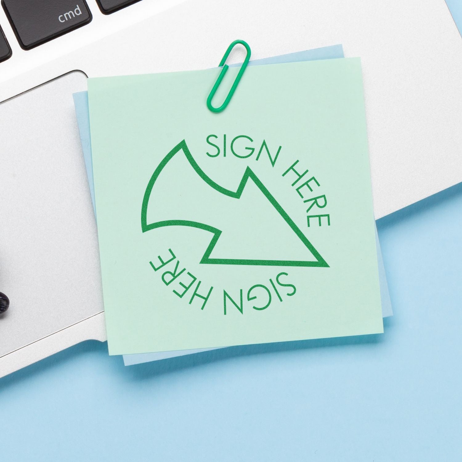 Green Sign Here sticky note clipped to documents on a laptop desk, office paperwork approval concept.