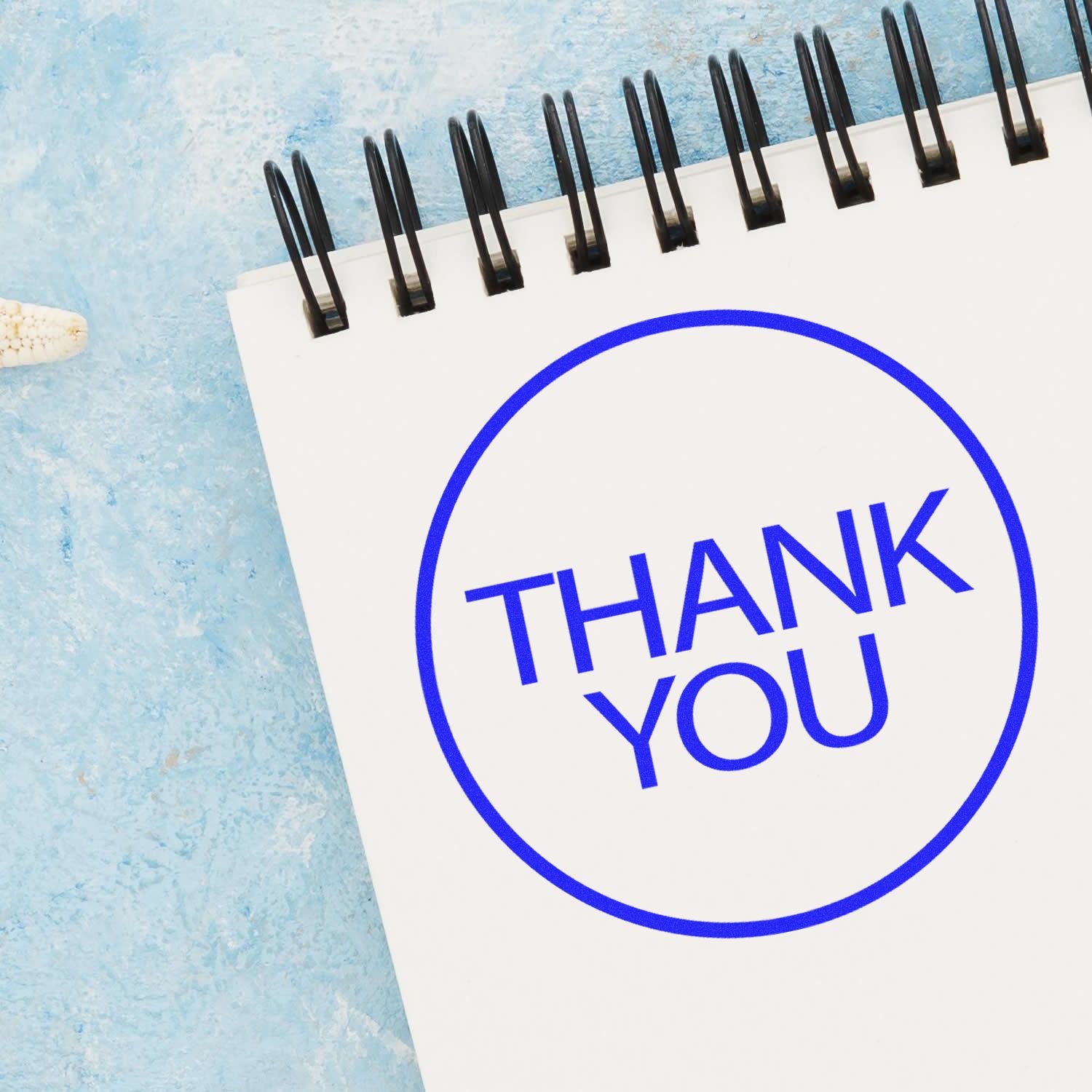 Spiral notebook with blue Thank You message on textured blue background, business gratitude concept.