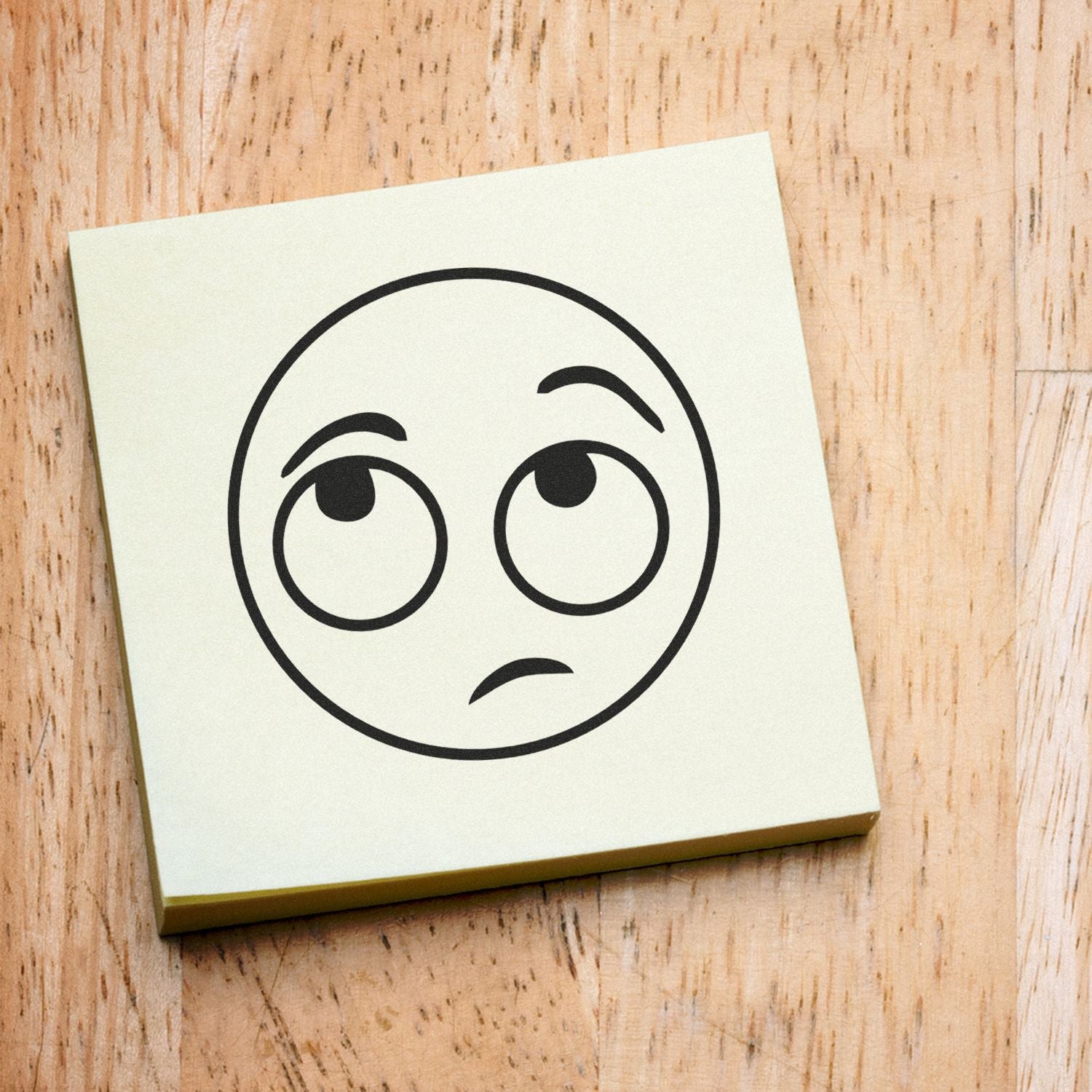 Confused face emoji sticky note on a wooden background, simple emoji icon illustration.