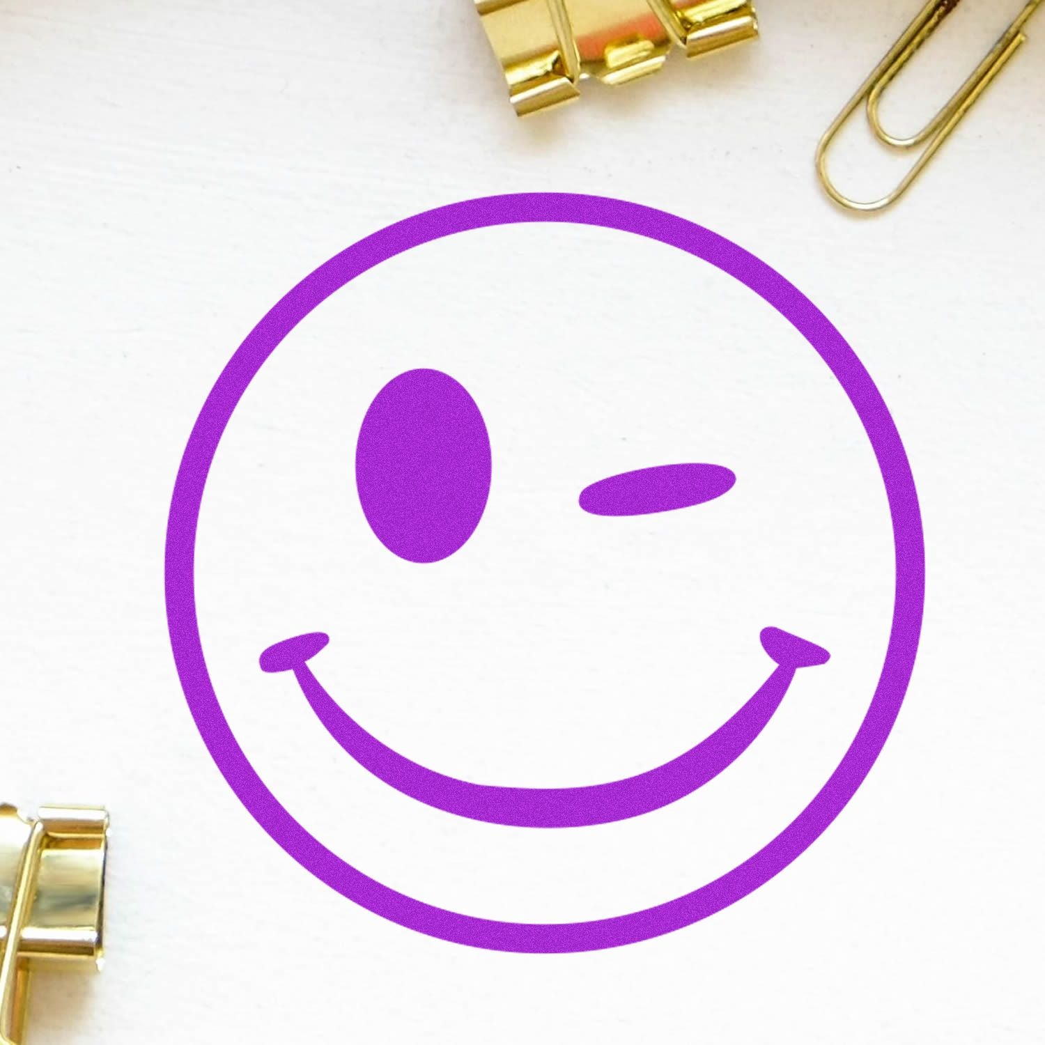 Purple winking smiley face icon on white background with gold paper clips, fun minimalist stationery design.