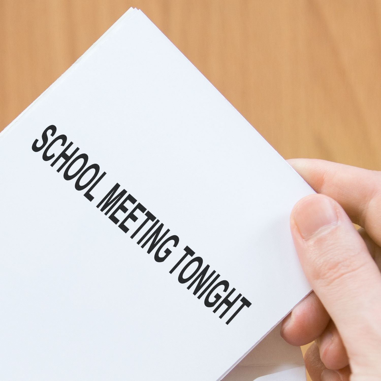 Hand holding a school meeting tonight flyer with bold black text on white paper, education event announcement.