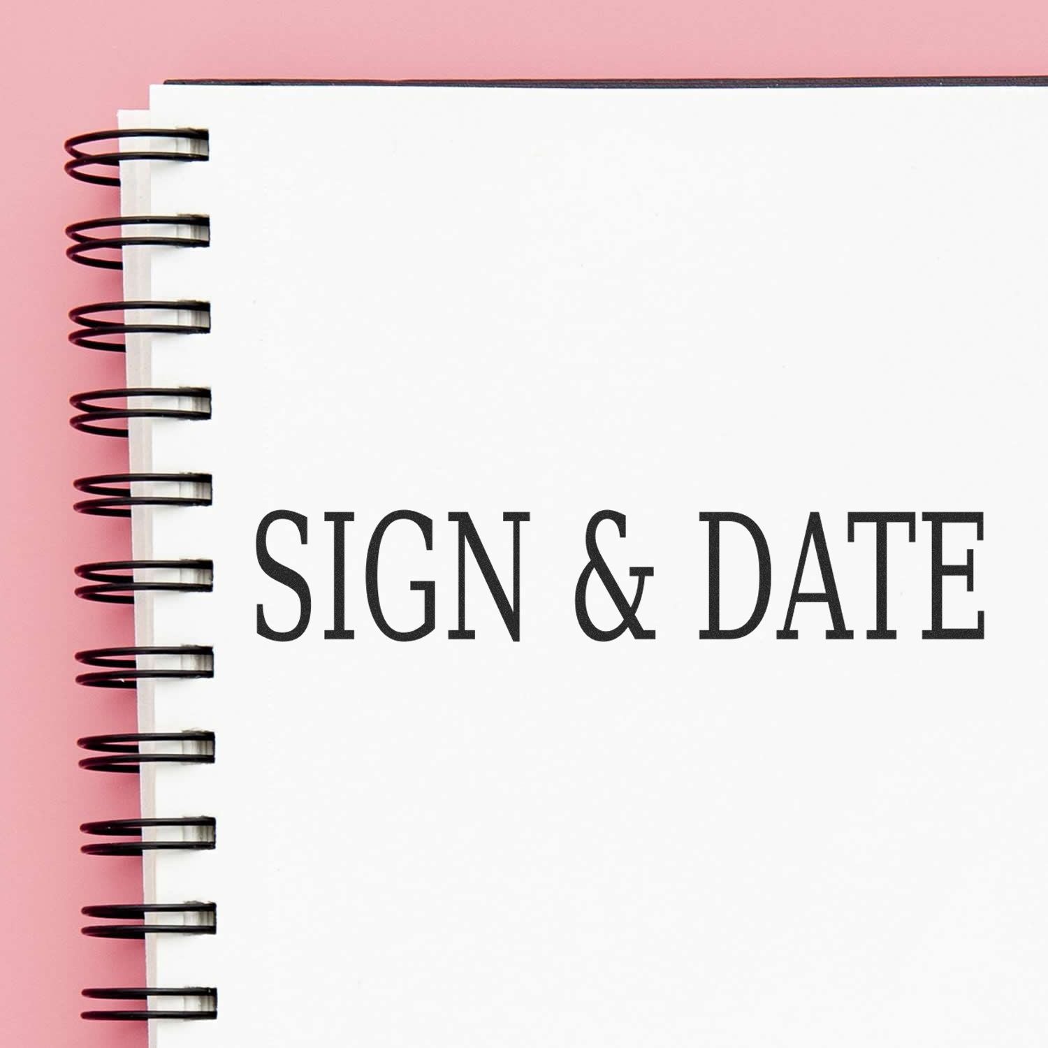 Spiral notebook with SIGN & DATE text on a pink background, minimalist office or planning concept.