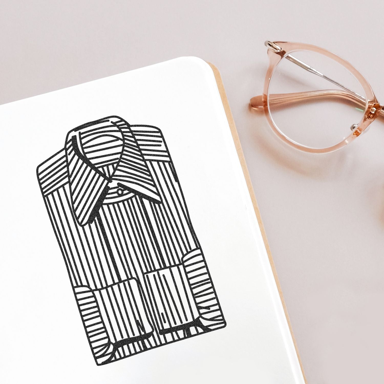 Minimalist fashion sketch on a notebook beside rose gold eyeglasses, stylish flat lay stationery design.