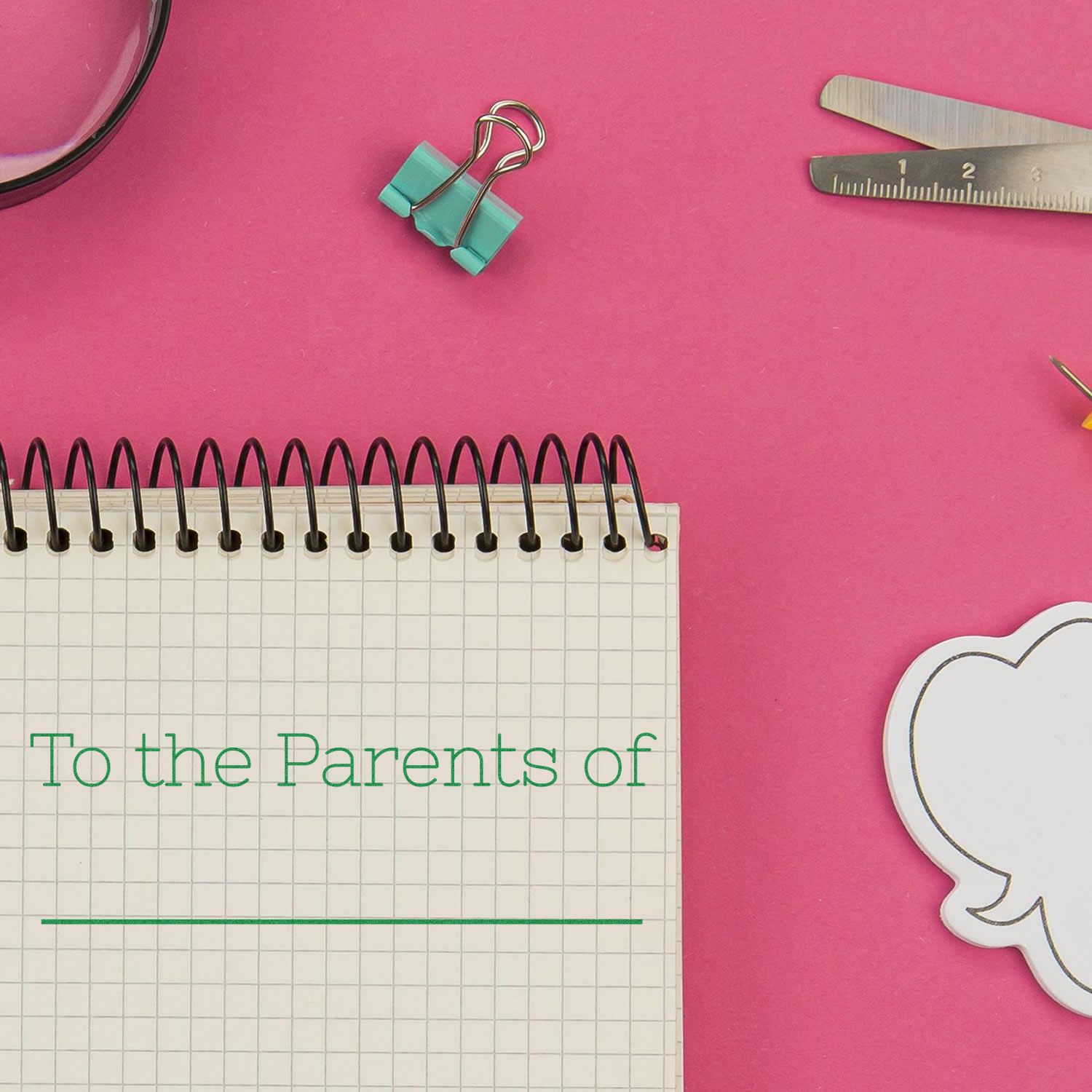 Flat lay of a spiral notebook with To the Parents of text on a pink desk with stationery supplies.