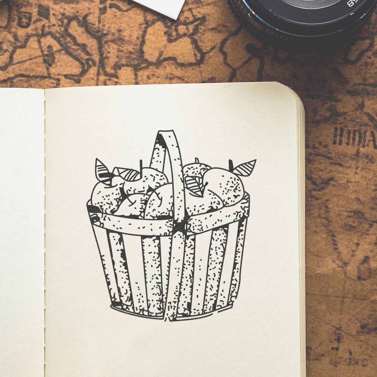 Hand-drawn cupcake illustration in an open sketchbook on a vintage map background with a camera lens in the corner.