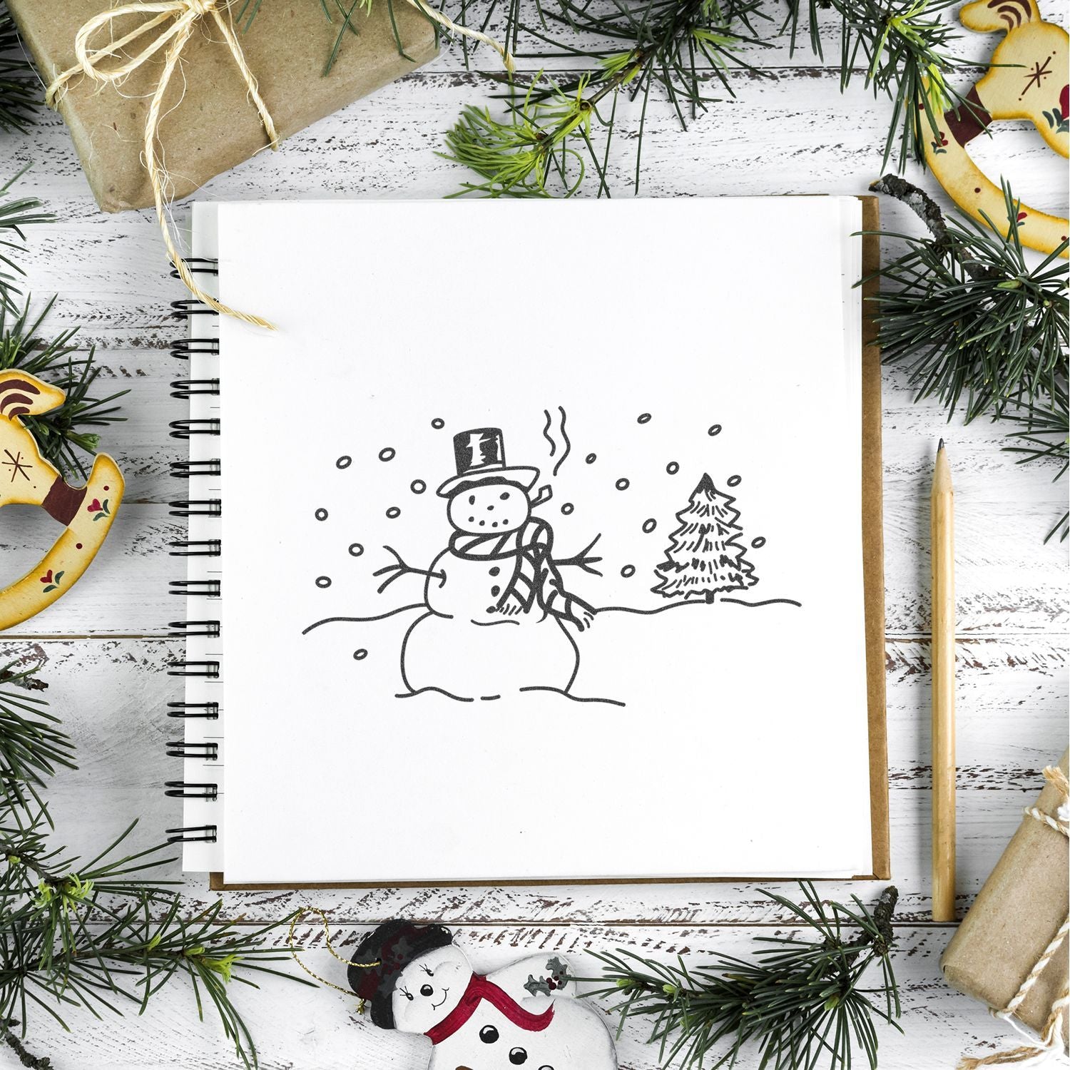 Holiday sketchbook with hand-drawn snowman, Christmas pine branches, wrapped gifts, and festive wooden ornaments.