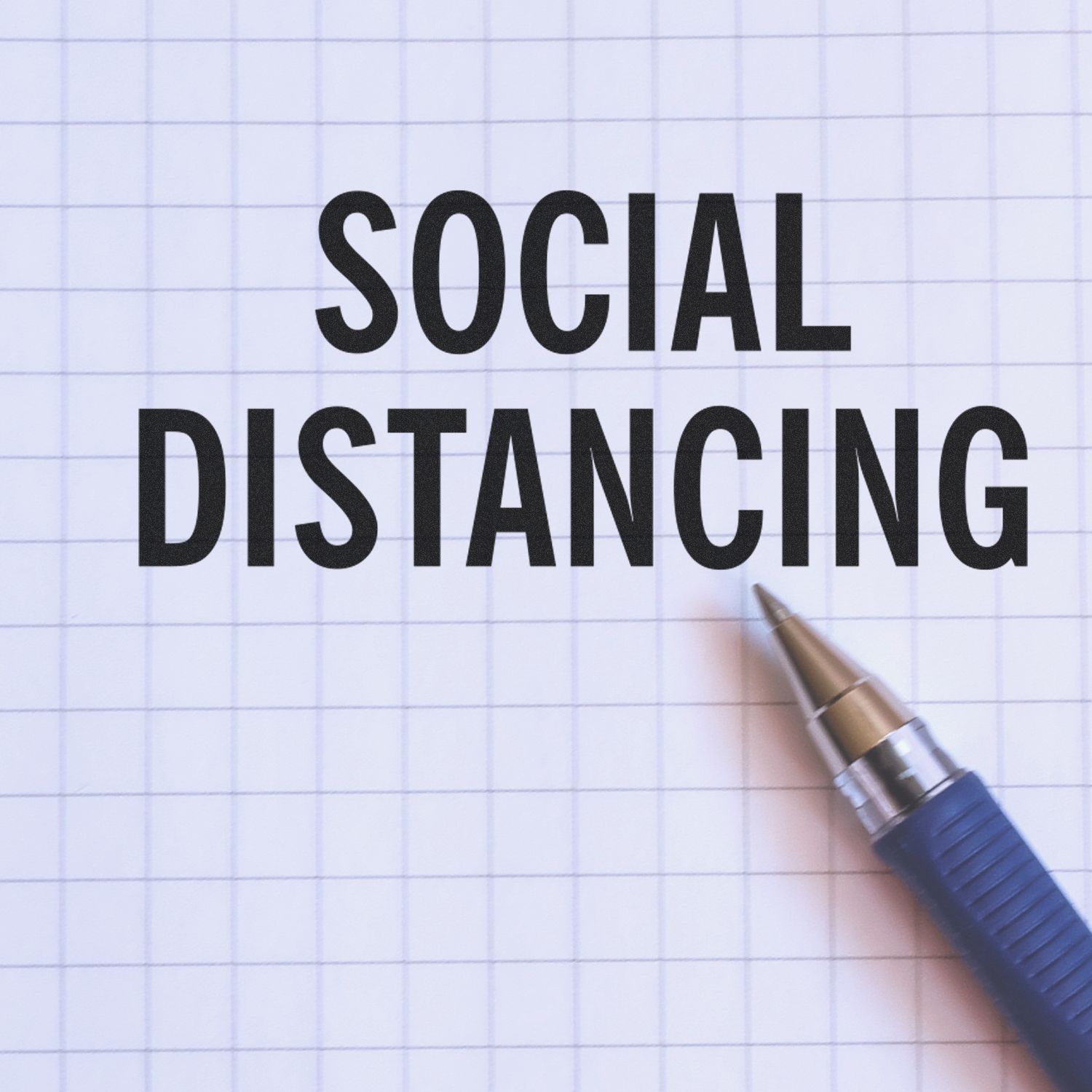 Social distancing text on graph paper with a pen, concept of social distancing and public health safety.