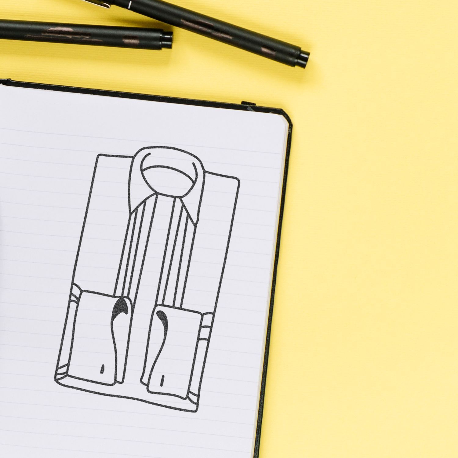 Notebook with a zipper design sketch and black pens on a yellow background