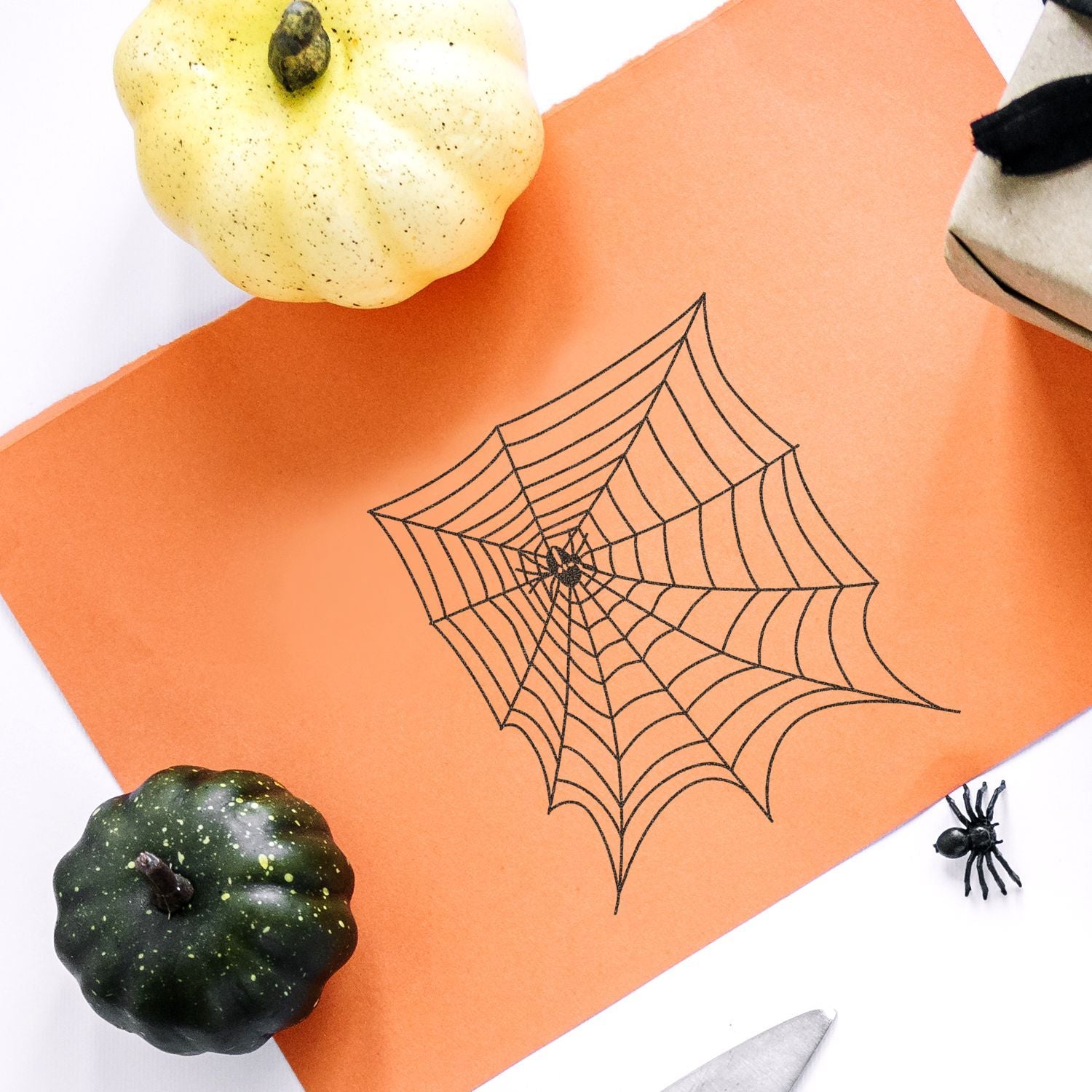 Halloween spider web craft on orange paper with decorative pumpkins and a toy spider, festive autumn Halloween flat lay.
