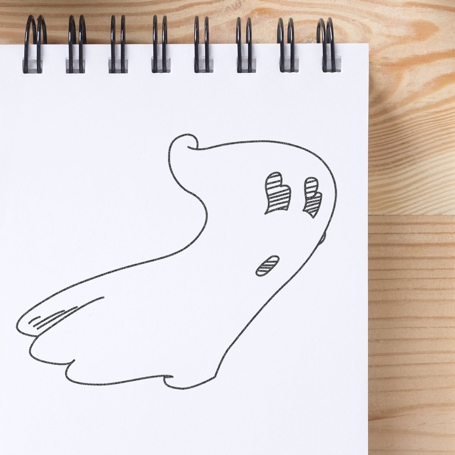 Simple hand-drawn ghost doodle on spiral notebook paper on a wooden desk